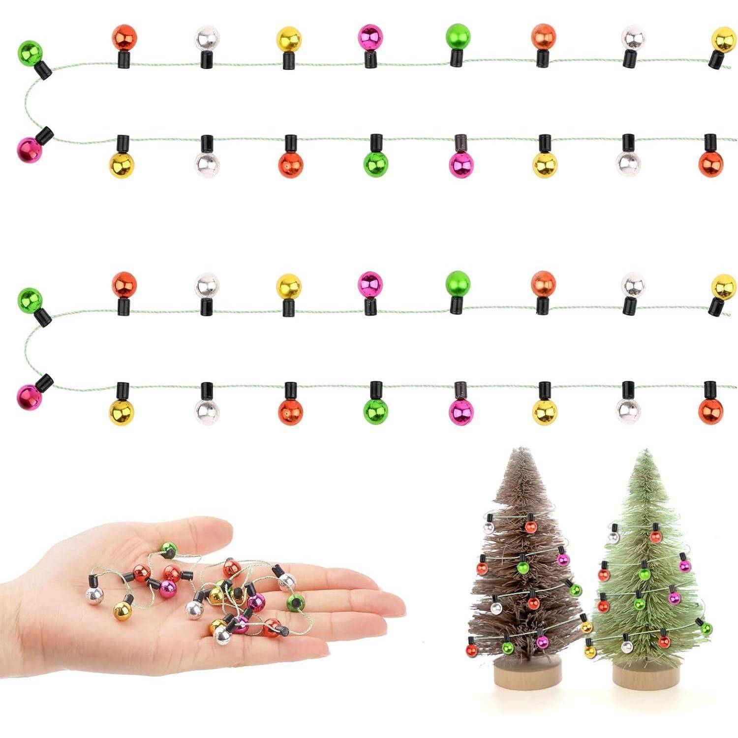 Bunte Weihnachtsbeleuchtung und kleine festliche Dekorationen; Hand, die Christbaumschmuck hält; zwei kleine dekorierte Tischbäume mit mehrfarbigen Weihnachtskugeln.