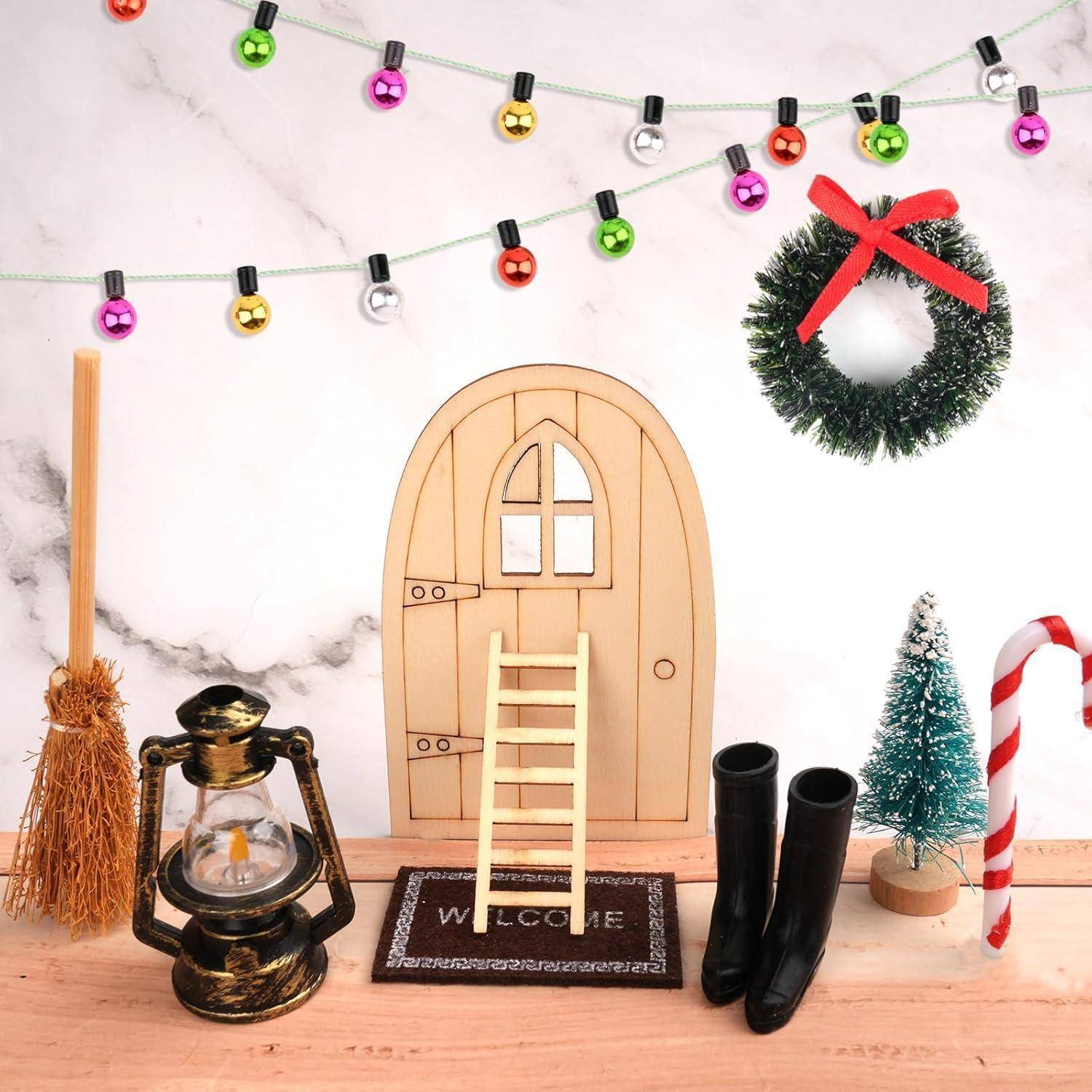Eine festliche Anordnung mit einer kleinen Holztür, einer Leiter, einem Kranz, einem Besen, einer Laterne, Stiefeln und Weihnachtsbeleuchtung, die vor einer marmorartigen Wand steht.