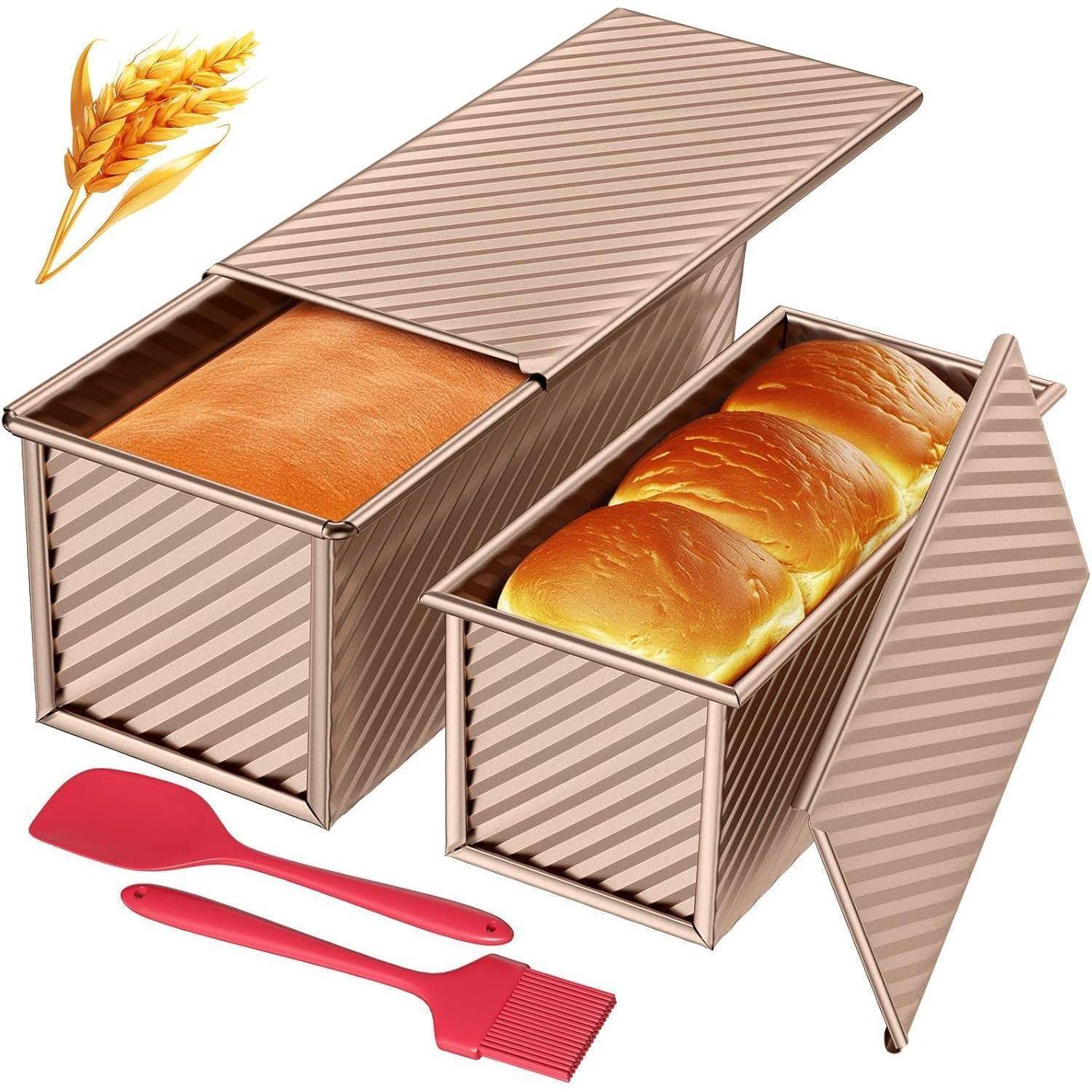 Zwei rechteckige, gestreifte Brotbackformen mit offenen Deckeln; eine enthält ein Brot, die andere drei Brötchen. Dazu gehören ein roter Pfannenwender und ein Pinsel.