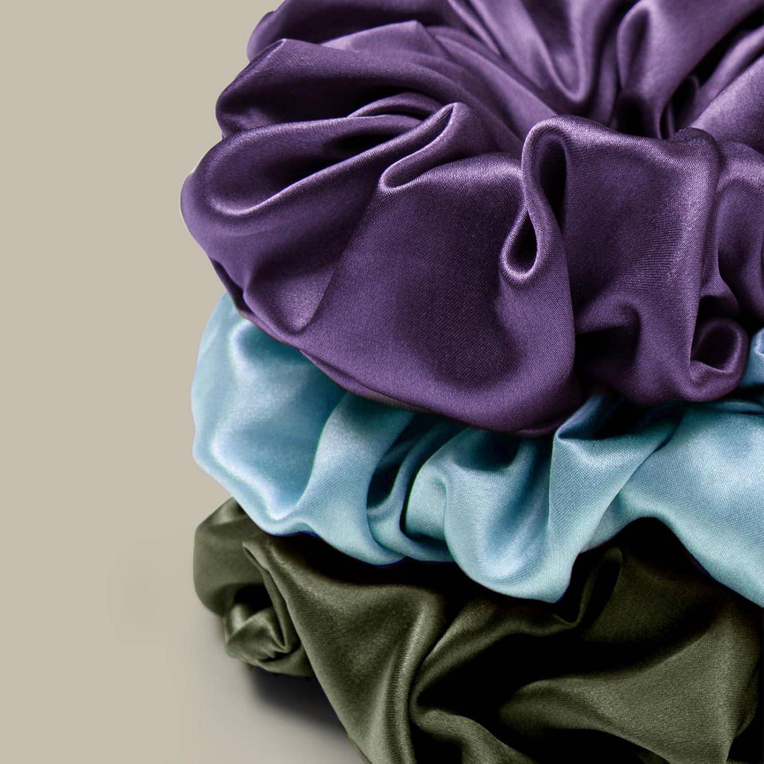 Ein Stapel von drei Scrunchies in den Farben Lila, Blau und Olivgrün, die ihre Satintextur und das voluminöse gerüschte Aussehen zur Schau stellen.