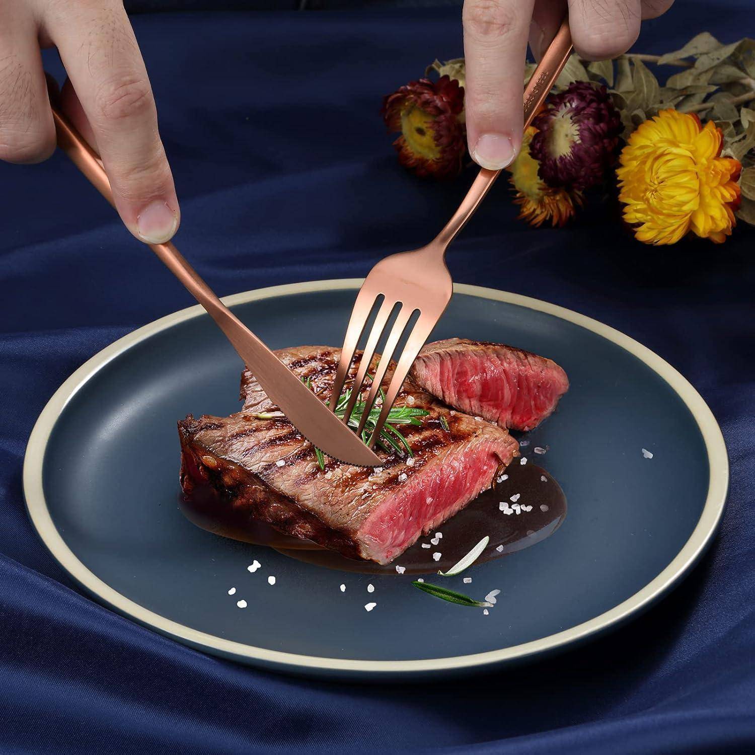 Eine Person schneidet ein medium-rare Steak auf einem blauen Teller mit Gabel und Messer. Im Hintergrund sind leuchtend bunte Blumen.