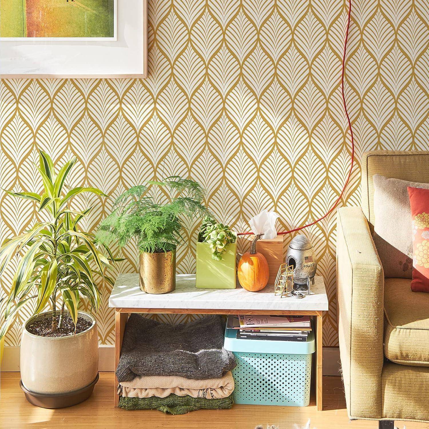 Eine gemütliche Ecke im Wohnzimmer mit einer kleinen Bank, auf der Pflanzen, Bücher und eine kleine Lampe stehen, vor einer gemusterten Wand und neben einem gepolsterten Sessel.