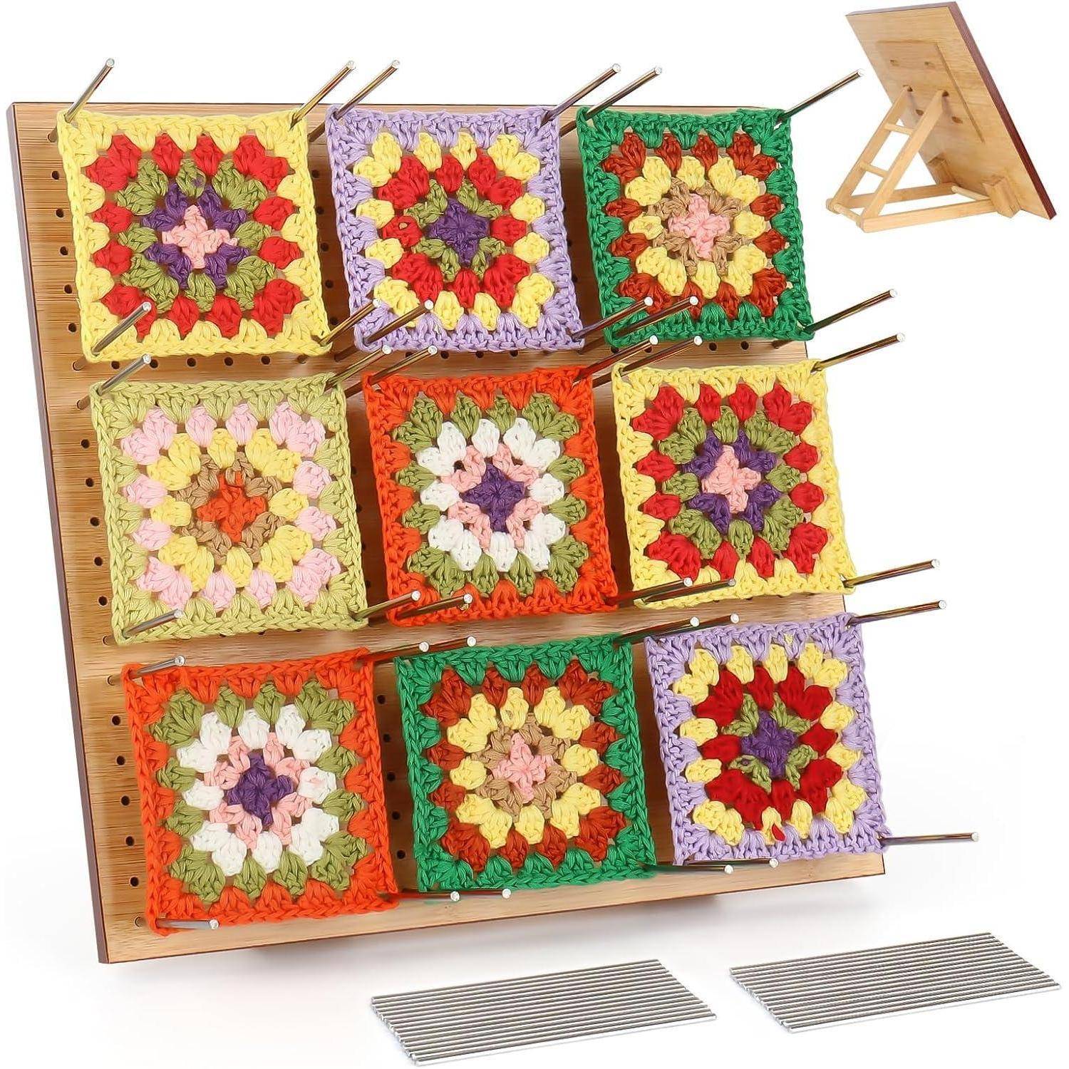 Häkelblockierungsbrett mit neun farbenfroh gepinnten Granny Squares, wobei jedes Quadrat einzigartige Muster und Farben aufweist, auf einem Ständer befestigt.