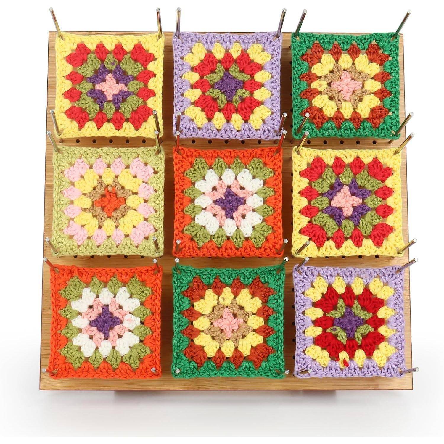Ein quadratisches Display, das neun farbenfrohe gehäkelte Granny Squares mit verschiedenen Mustern und Farben auf einem Holzbrett mit Metallhaken zeigt.