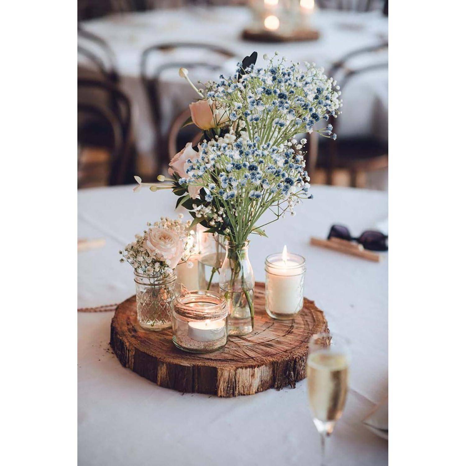 Ein rustikales Holz-Mittelstück mit zarten weißen und blauen Blumen in Gläsern, umgeben von brennenden Kerzen auf einer weißen Tischdecke.