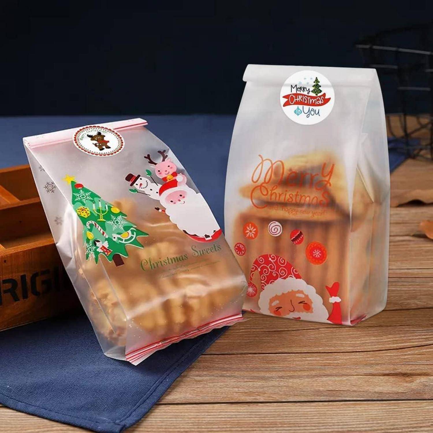 Zwei weihnachtlich gestaltete Leckertüten mit festlichen Mustern, darunter eine Weihnachtsmann- und eine Christbaumdarstellung, auf einem Holztisch mit blauer Decke.