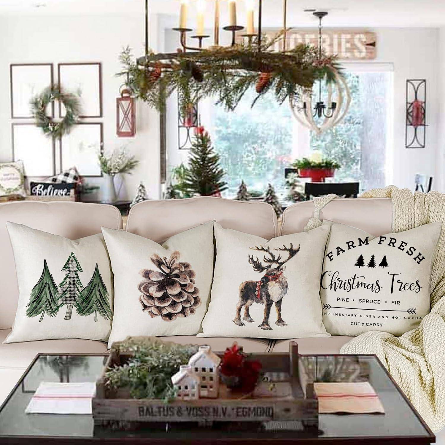 Ein gemütliches Wohnzimmer, weihnachtlich dekoriert mit festlichen Kissenbezügen, die Bäume, einen Tannenzapfen und ein Rentier auf einem weißen Sofa zeigen.