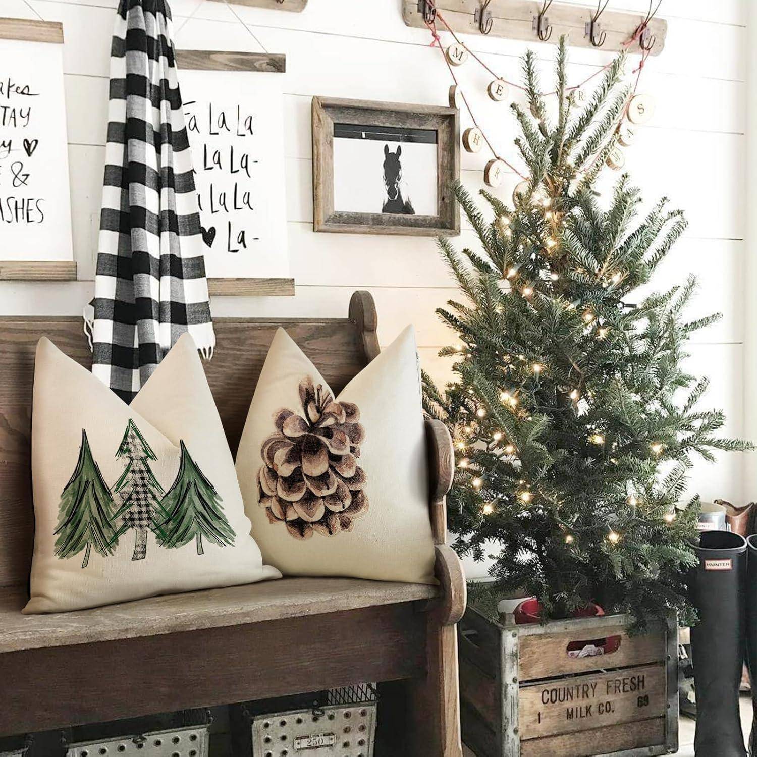 Ein gemütliches Zimmer im rustikalen Stil zeigt einen kleinen geschmückten Weihnachtsbaum, gerahmte festliche Schilder und Kissen mit Baum- und Tannenzapfenmustern auf einer Holzbank.