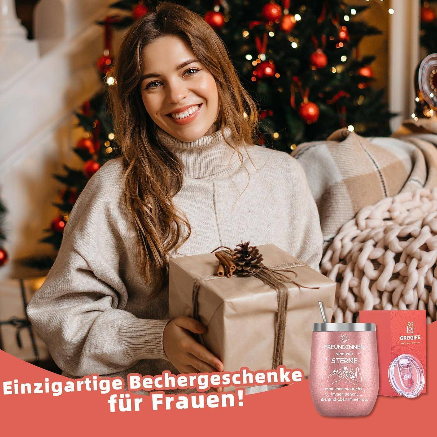 Eine lächelnde Frau in einem gemütlichen Pullover hält ein eingewickeltes Geschenk, umgeben von festlichen Weihnachtsdekorationen. Text auf Deutsch bewirbt Geschenkideen für Frauen.