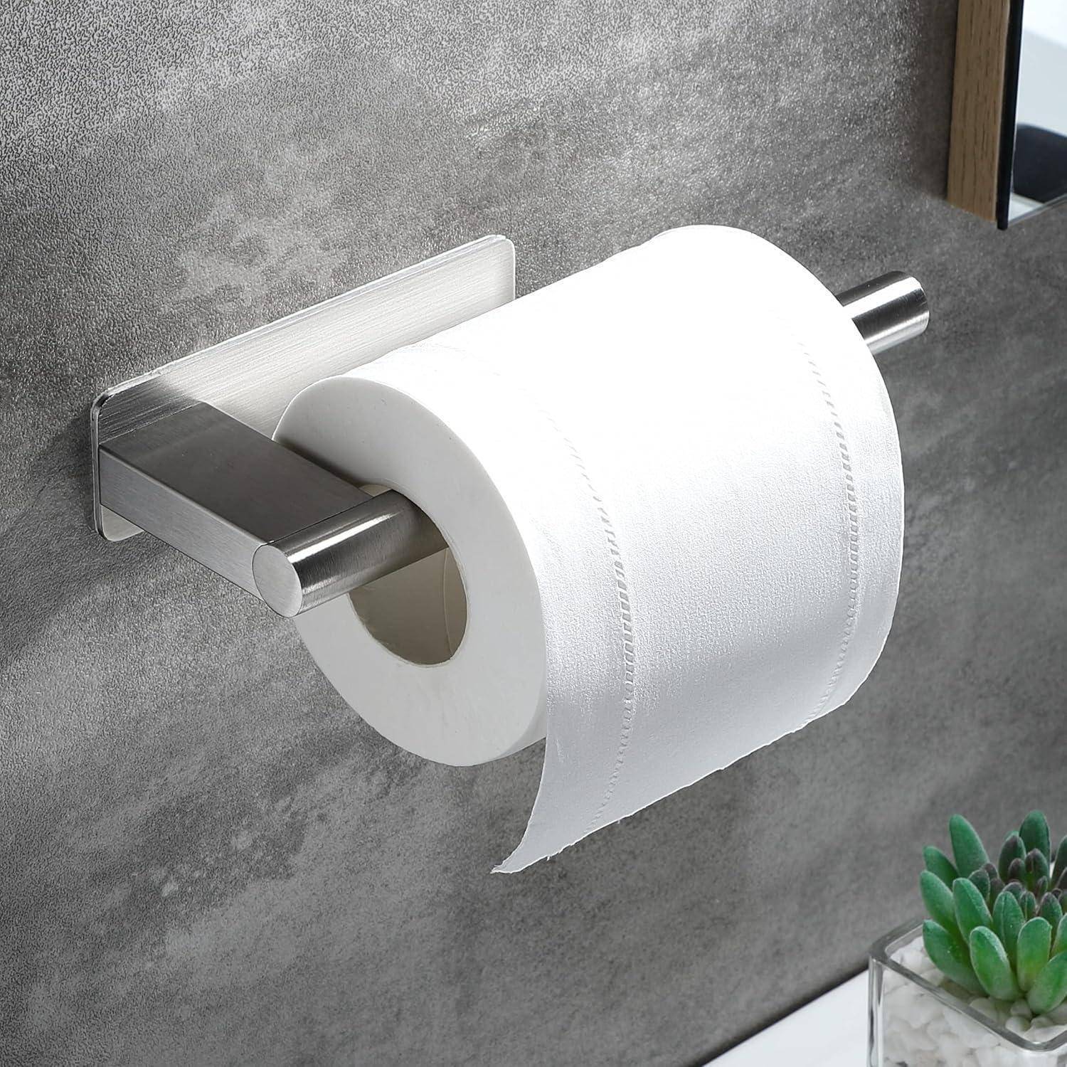 Eine Rolle Toilettenpapier ist an einem Metallhalter an einer grauen gefliesten Wand befestigt. Neben ihr ist eine kleine grüne Pflanze zu sehen.