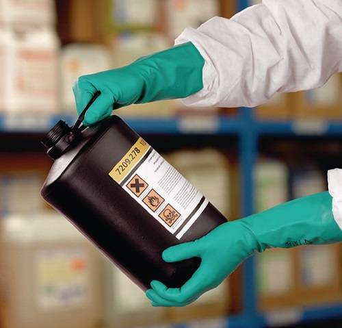 Behandschuhte Hände halten einen Chemikalienbehälter mit Gefahrensymbolen und der Nummer '7209-278', die Sicherheitsvorkehrungen in einer Laborumgebung anzeigen.