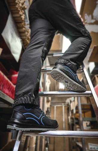 Eine Person mit schwarzen Turnschuhen mit blauen Akzenten klettert eine Metallleiter in einer Lagerumgebung mit gestapelten Kisten.