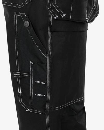 Nahaufnahme einer schwarzen Hose mit weißen Stickdetails, ausgestattet mit Vordertaschen, seitlichen Riemen und detaillierten Nahtarbeiten am Bein.