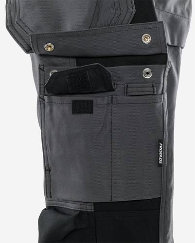 Eine Nahaufnahme von Arbeitshosen mit mehreren Taschen, Knöpfen und einem Klettverschluss-Überschlag, die für Praktikabilität und Bequemlichkeit beim Tragen von Werkzeugen konzipiert sind.