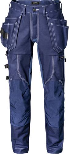 Eine Person trägt blaue Jeans mit weißen Nähten und Utility-Trägern und steht vor einem schwarzen Hintergrund.