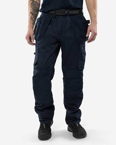 Eine Person trägt dunkelblaue Cargohosen mit mehreren Taschen und steht vor einem einfarbigen Hintergrund.