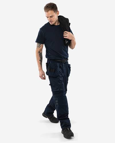 Eine Person in einem dunkelblauen Hemd und einer dunkelblauen Hose, die eine Jacke über der Schulter trägt und läuft. Sie hat Tattoos auf ihrem linken Arm.