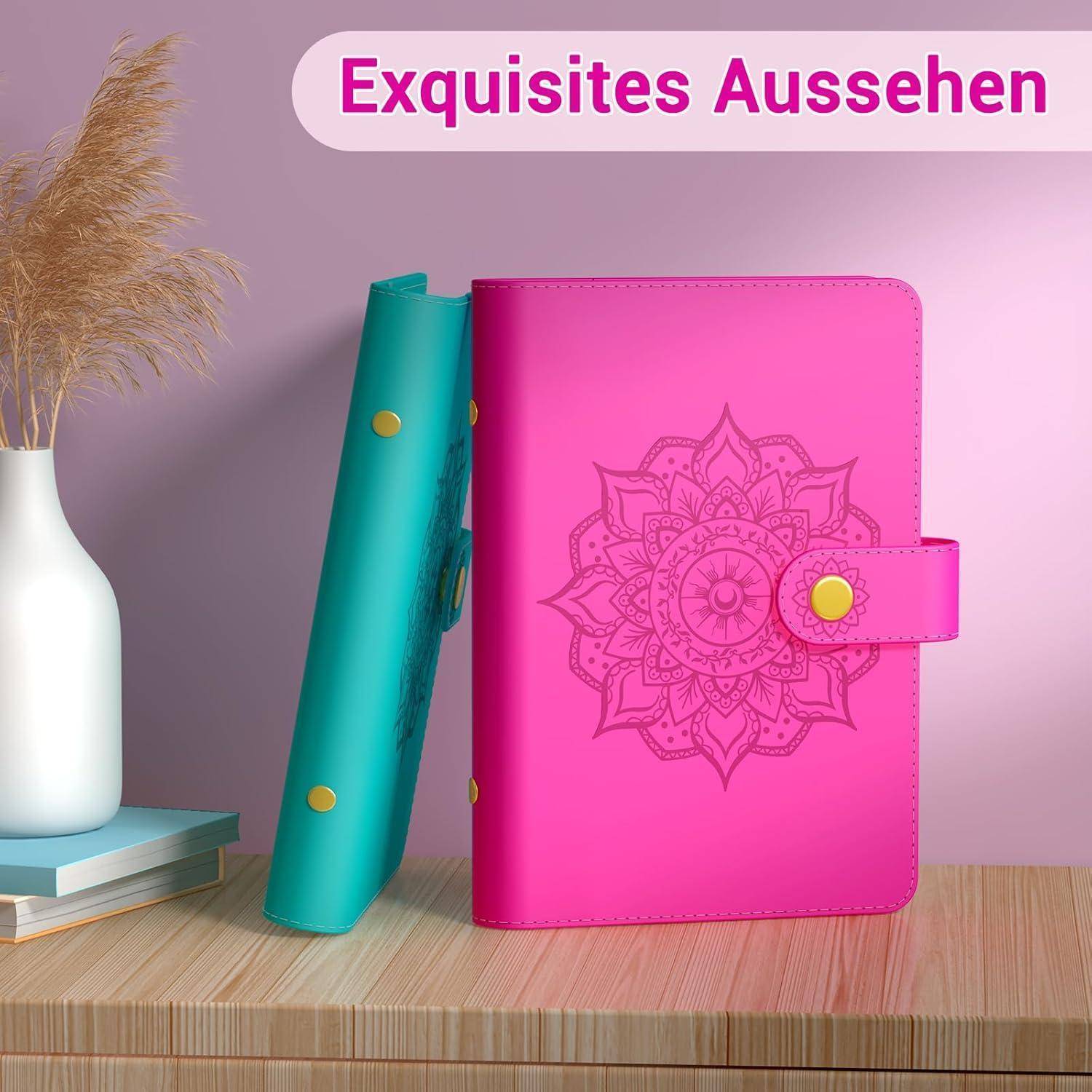 Ein rosa Notizbuch mit einem floralen Mandala-Muster steht aufrecht auf einer Holzoberfläche neben einem türkisfarbenen Notizbuch und einer weißen Vase mit getrockneten Gräsern. Deutscher Text oben liest sich 