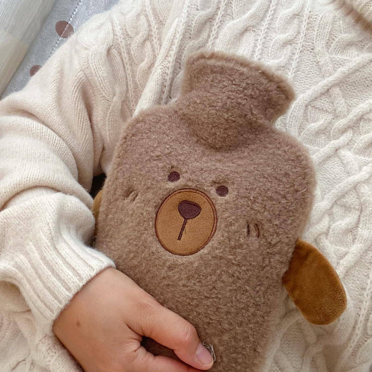Eine Person trägt einen gestrickten Pullover und hält eine weiche Wärmflasche mit Teddybären-Motiv, was Wärme und Geborgenheit vermittelt.