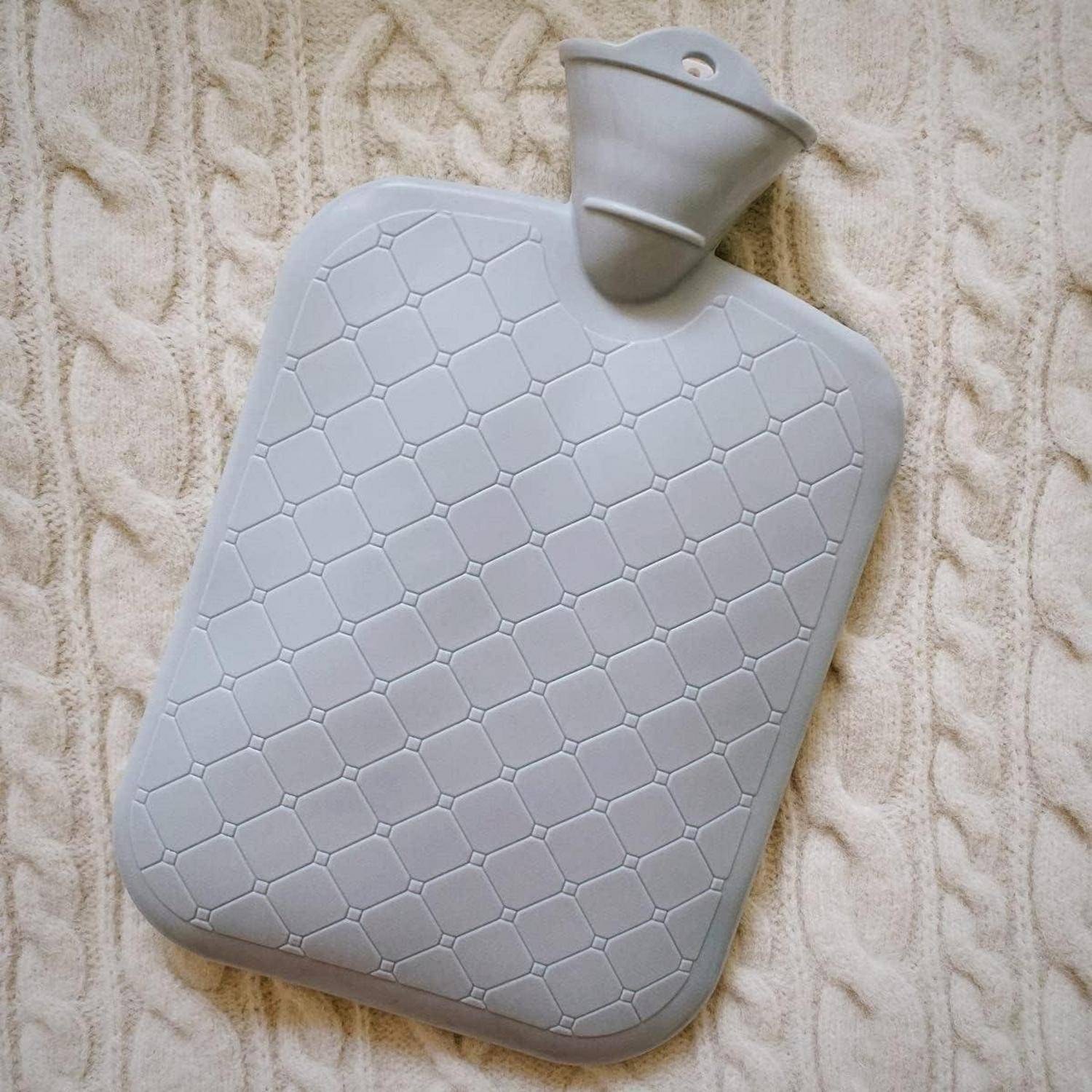 Eine graue, strukturierte Wärmflasche mit Rautenmuster, die auf einem gestrickten Stoffhintergrund ruht.