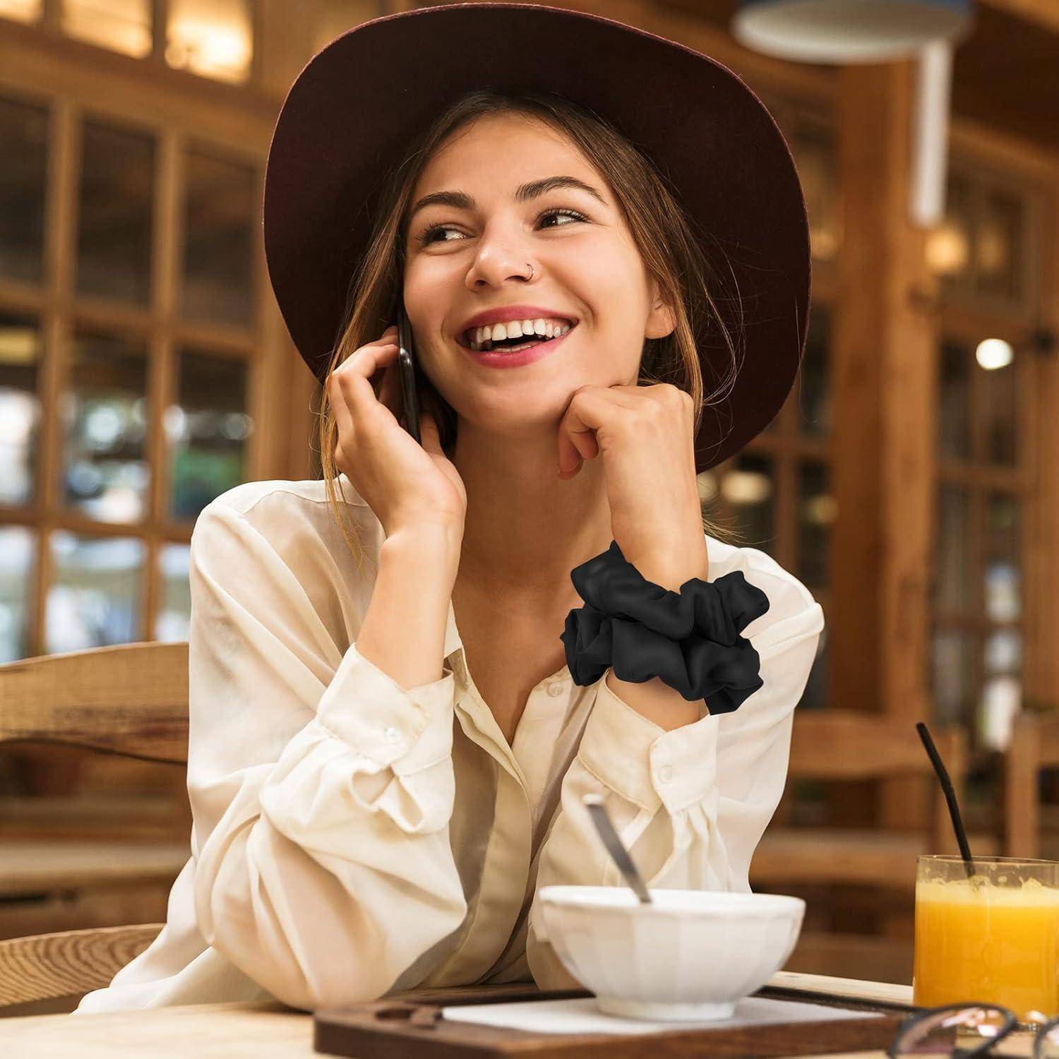 Eine Frau mit Hut und weißer Bluse lächelt, während sie an einem Cafétisch sitzt, mit einem Glas Orangensaft und einer kleinen Pflanze im Hintergrund.