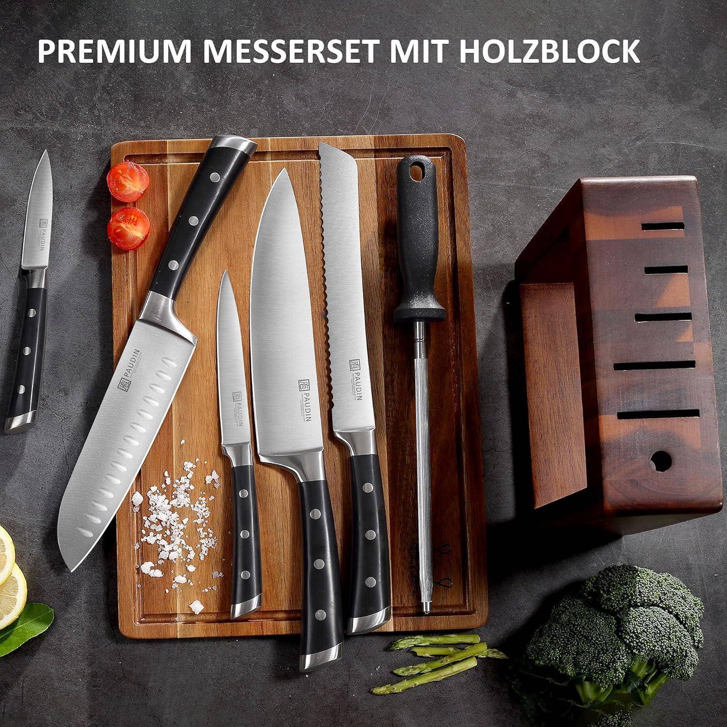 Ein hochwertiges Messerset auf einem Holzblock umfasst verschiedene Messer und einen Wetzstahl, umgeben von Gemüse auf einer Küchenarbeitsplatte.
