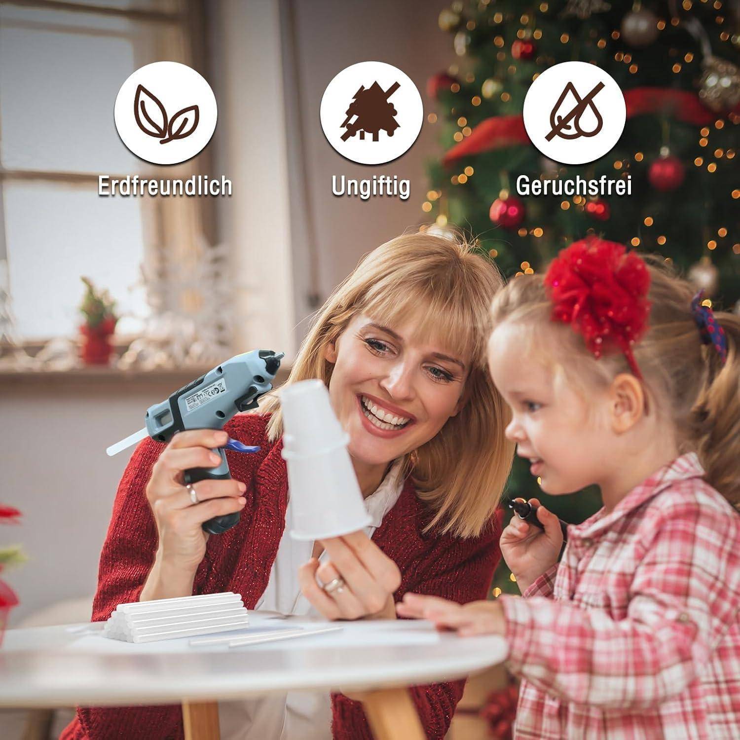 Eine Frau hilft einem Kind, eine Heißklebepistole zu verwenden, wobei sie betont, dass sie 'umweltfreundlich', 'ungiftig' und 'geruchlos' ist, mit Weihnachtsdekoration im Hintergrund.