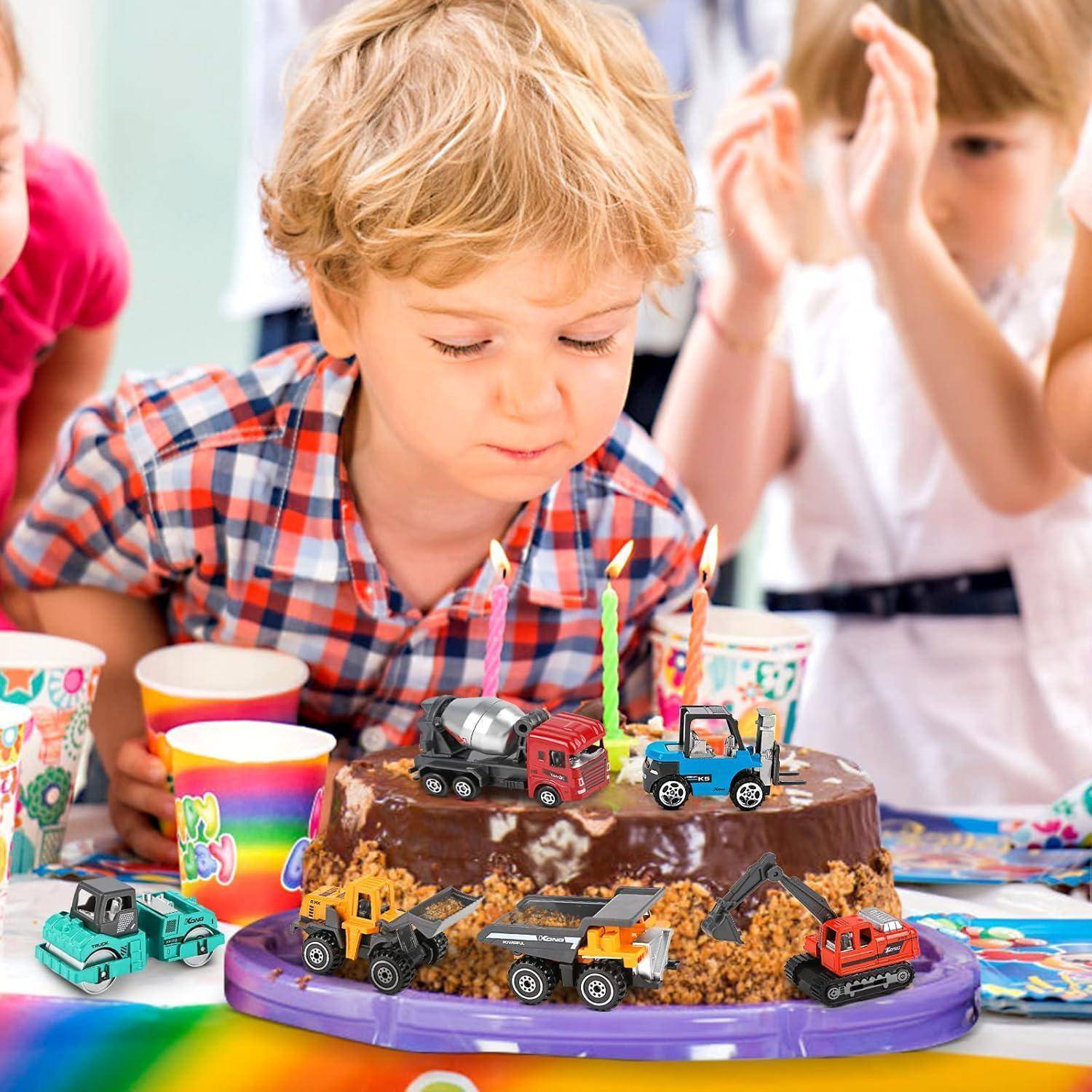 Ein Kind in einem Karohemd betrachtet eine Geburtstagstorte, die mit Spielzeug-Baufahrzeugen und brennenden Kerzen verziert ist und von bunten Bechern umgeben ist.