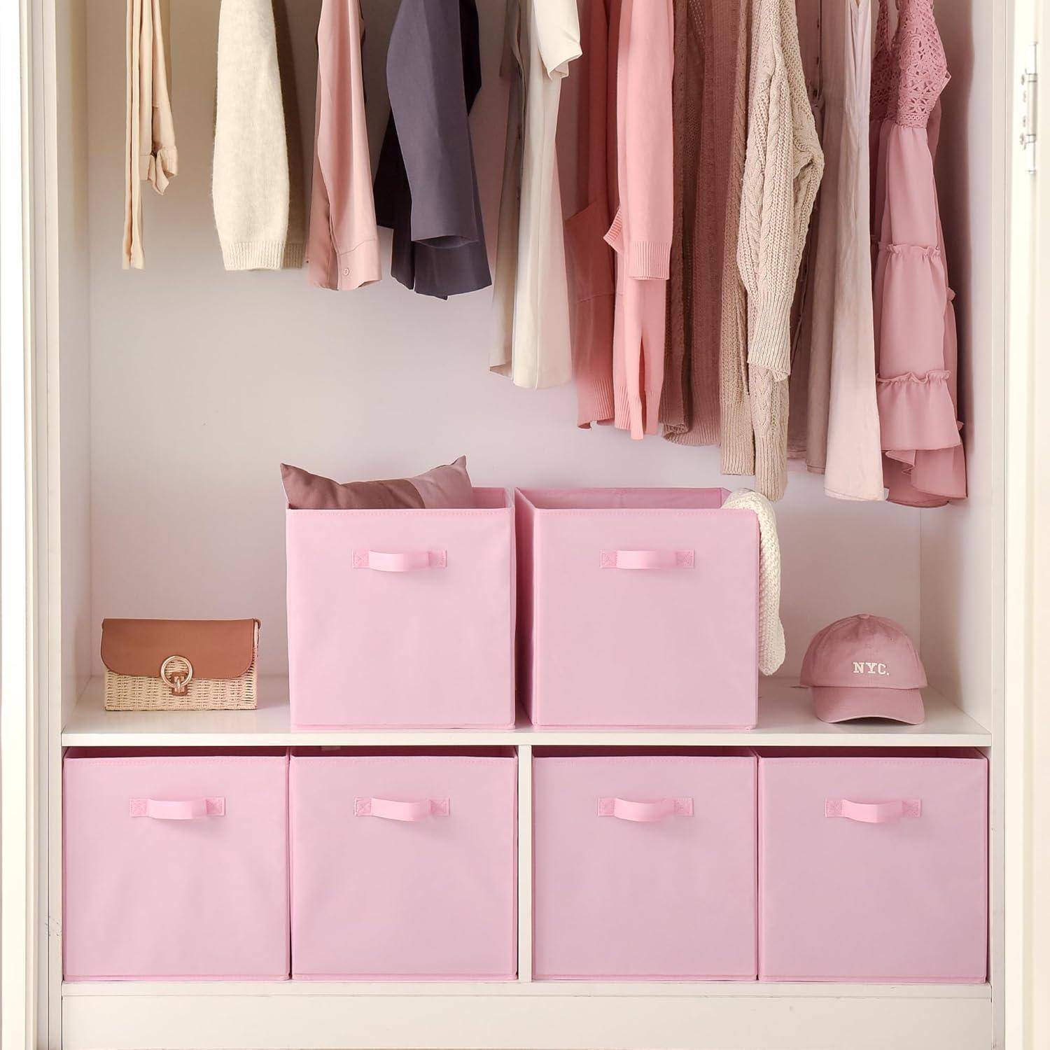 Ein ordentlich aufgeräumter Kleiderschrank mit rosa Aufbewahrungsboxen auf dem Regal und Kleidungsstücken in sanften Pastelltönen, die daran hängen. Rechts liegt ein Hut und eine kleine Tasche.