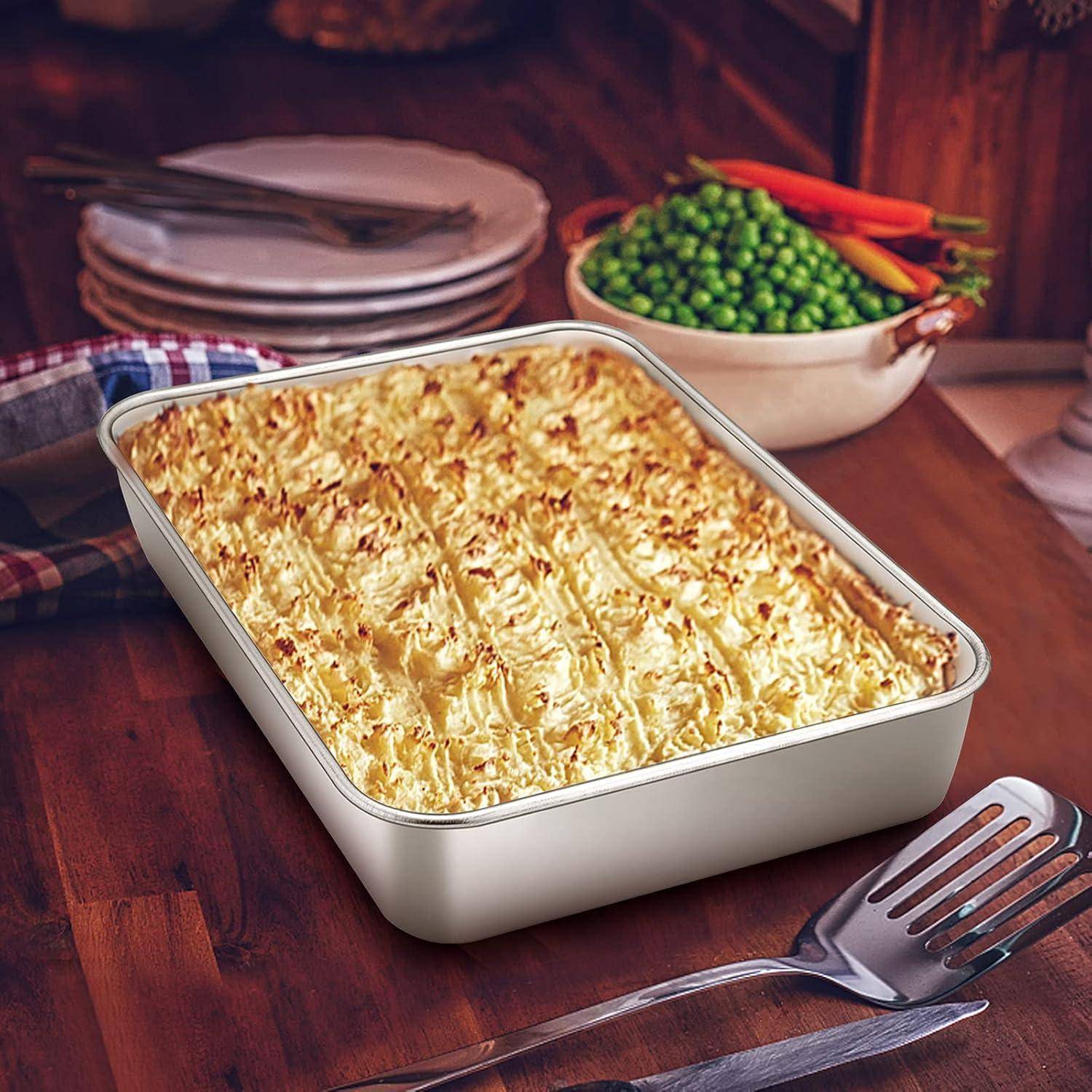 Eine gebackene Shepherds Pie in einer rechteckigen Form auf einem Holztisch, mit Tellern, einem gelochten Pfannenwender und einer Schüssel mit Erbsen und Karotten in der Nähe.