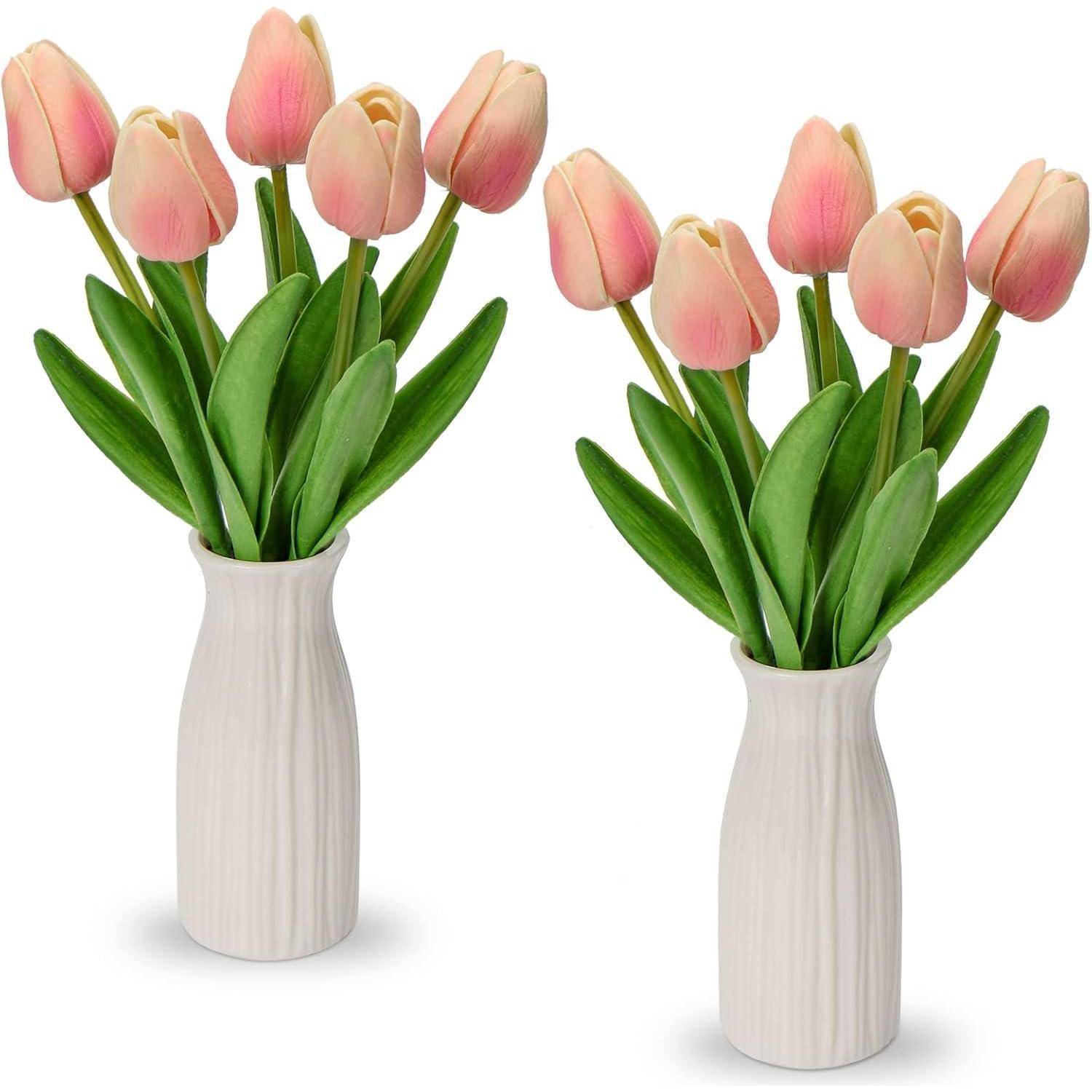 Zwei weiße Vasen auf weißem Hintergrund, die jeweils rosa Tulpen mit grünen Blättern enthalten und eine Blumenarrangement präsentieren.