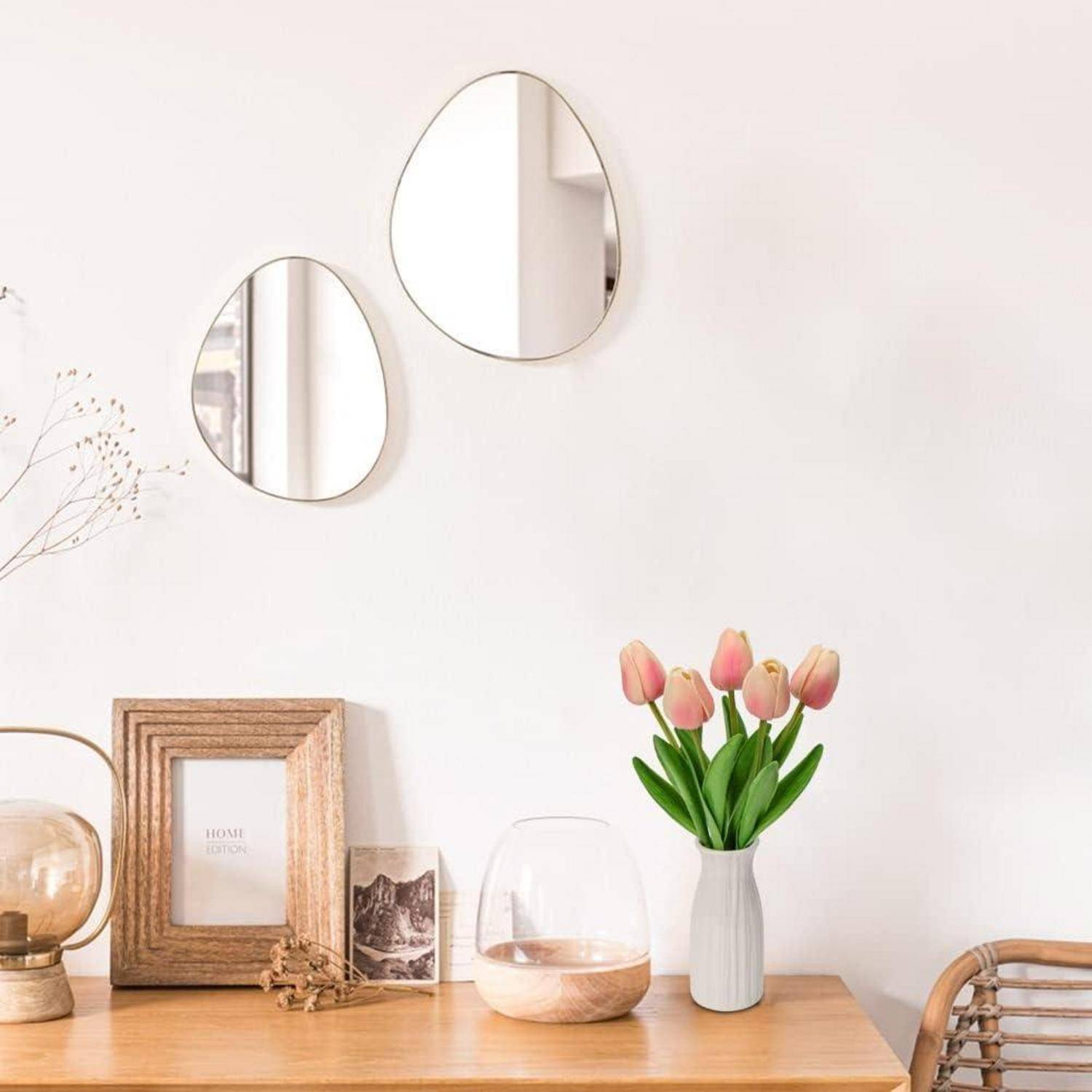 Ein minimalistischer Holzschreibtisch mit einer Vase mit rosa Tulpen, dekorativen Spiegeln und einem kleinen gerahmten Foto, der eine gemütliche, moderne Atmosphäre schafft.