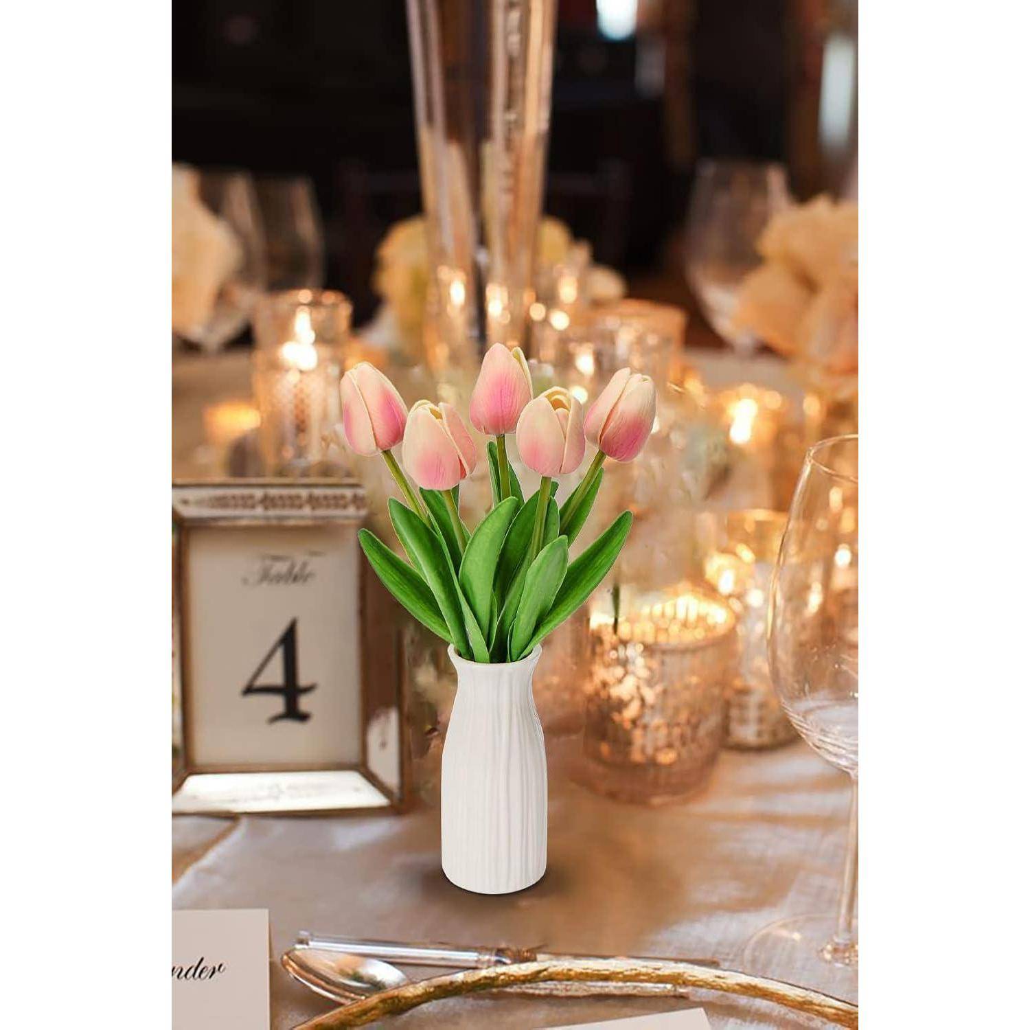 Ein für eine Veranstaltung dekorierter Tisch mit einer Vase voller rosa Tulpen, Kerzen und einer Tischplatzkarte mit der Nummer 4.