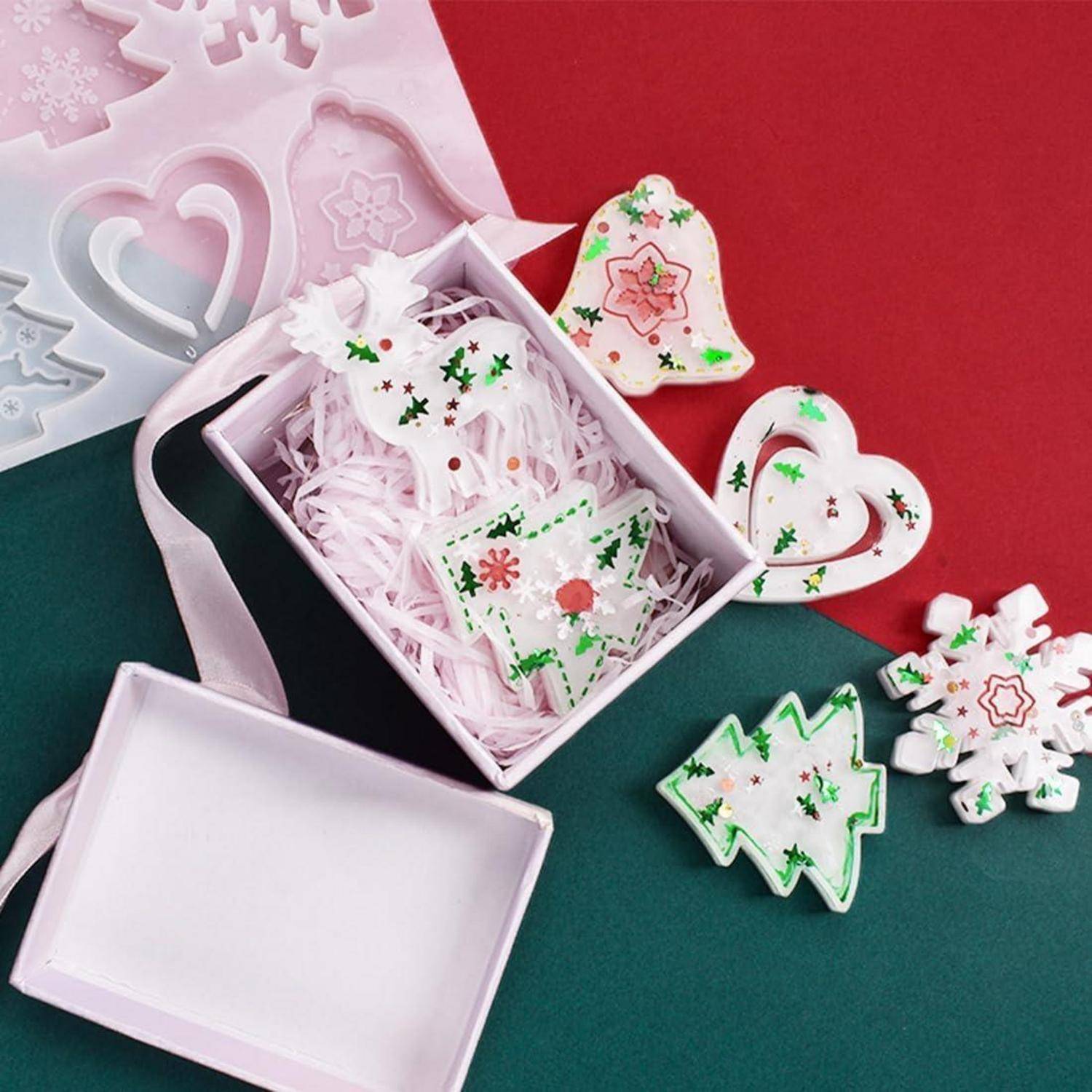 Eine Geschenkbox auf einem rot-grünen Hintergrund enthält weihnachtliche Plätzchen, die mit Zuckerguss verziert und in Form von Bäumen, Herzen und Glocken gestaltet sind.