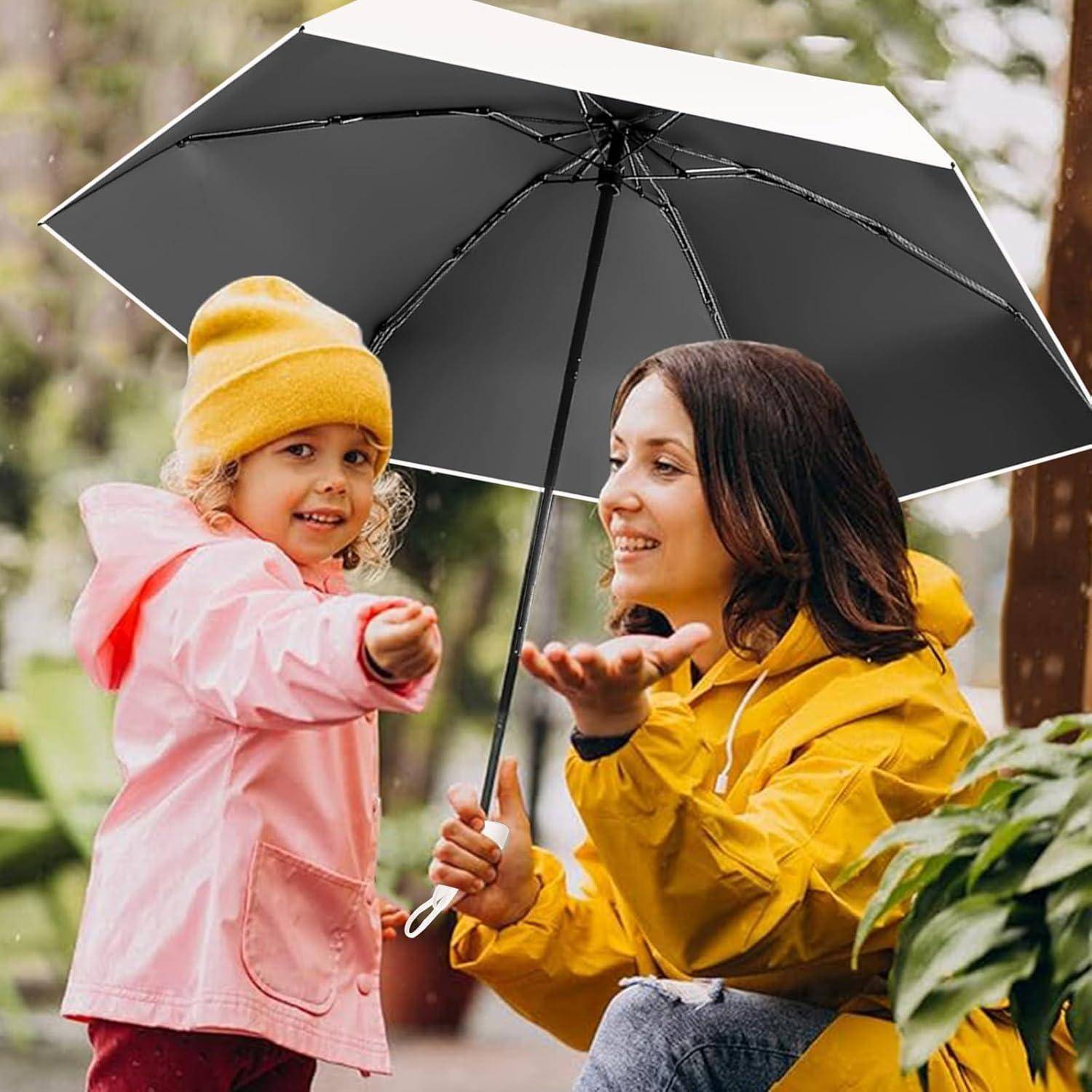 Eine Frau in einer gelben Jacke und ein Kind in einer pinken Jacke unter einem großen Regenschirm, die draußen an einem regnerischen Tag mit üppigem Grün lächeln.