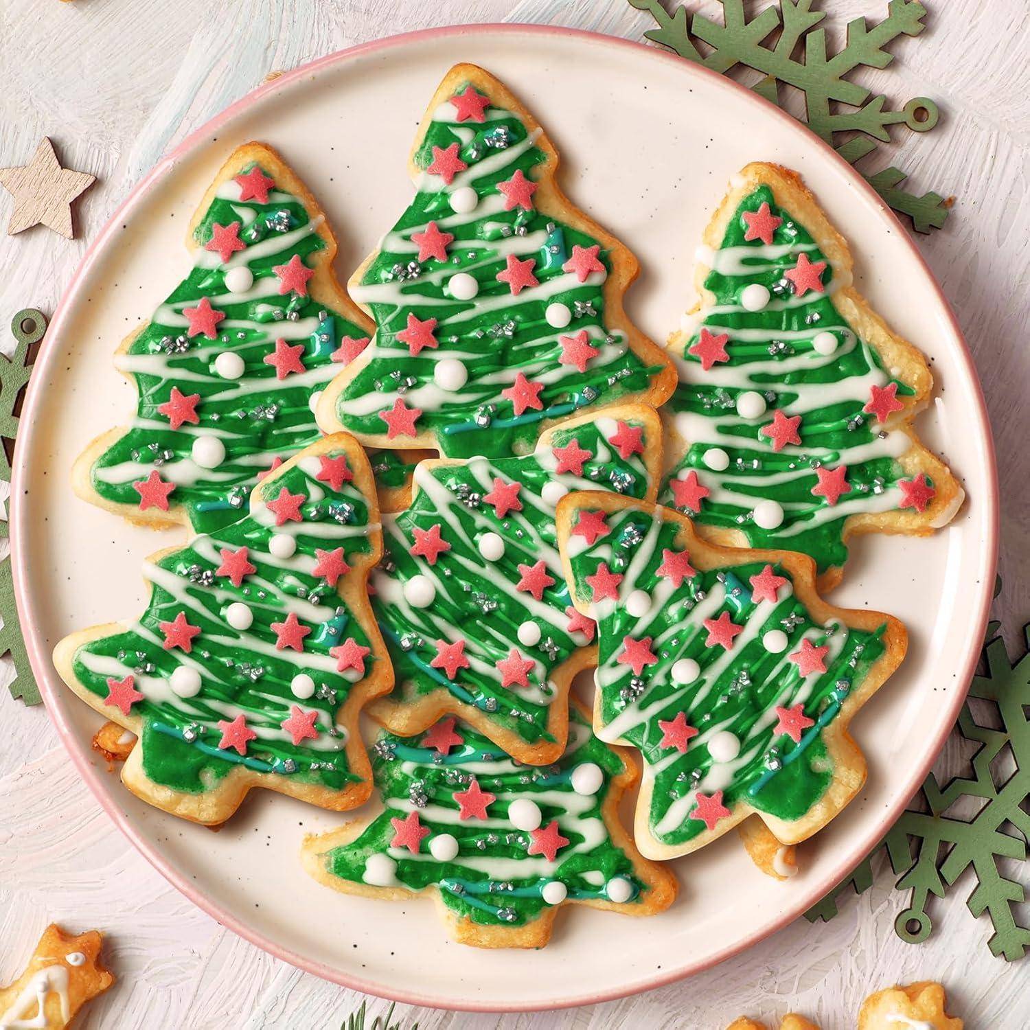 Ein Teller mit Weihnachtsbaumförmigen Plätzchen, verziert mit grüner Zuckerglasur, weißen Punkten und roten Sternen, festlich angerichtet.