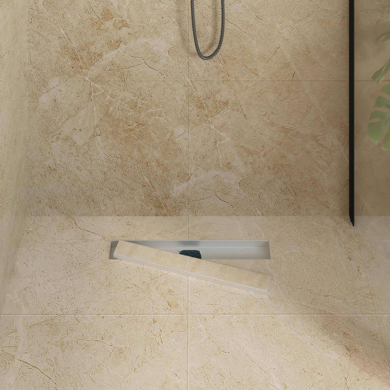 Ein beiger gefliester Duschboden mit einem rechteckigen Ablauf und einem hängenden Duschkopf, teilweise sichtbar, was auf ein minimalistisches Design hindeutet.