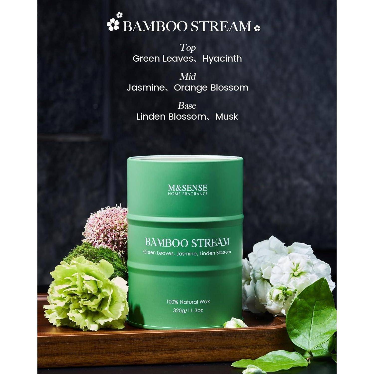 Grüne Kerze vor Blumen, beschriftet mit 'M&SENSE Home Fragrance', Duft 'Bamboo Stream' mit Noten von grünen Blättern, Jasmin und Moschus.