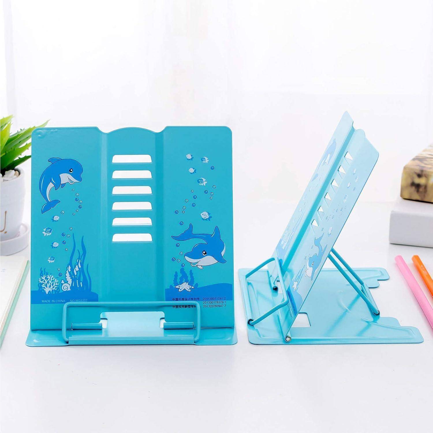 Blaue Buchständer mit Delfin-Illustrationen auf einem weißen Schreibtisch, verwendet zum aufrechten Halten von Büchern oder Tablets, umgeben von Stiften und Pflanzen.