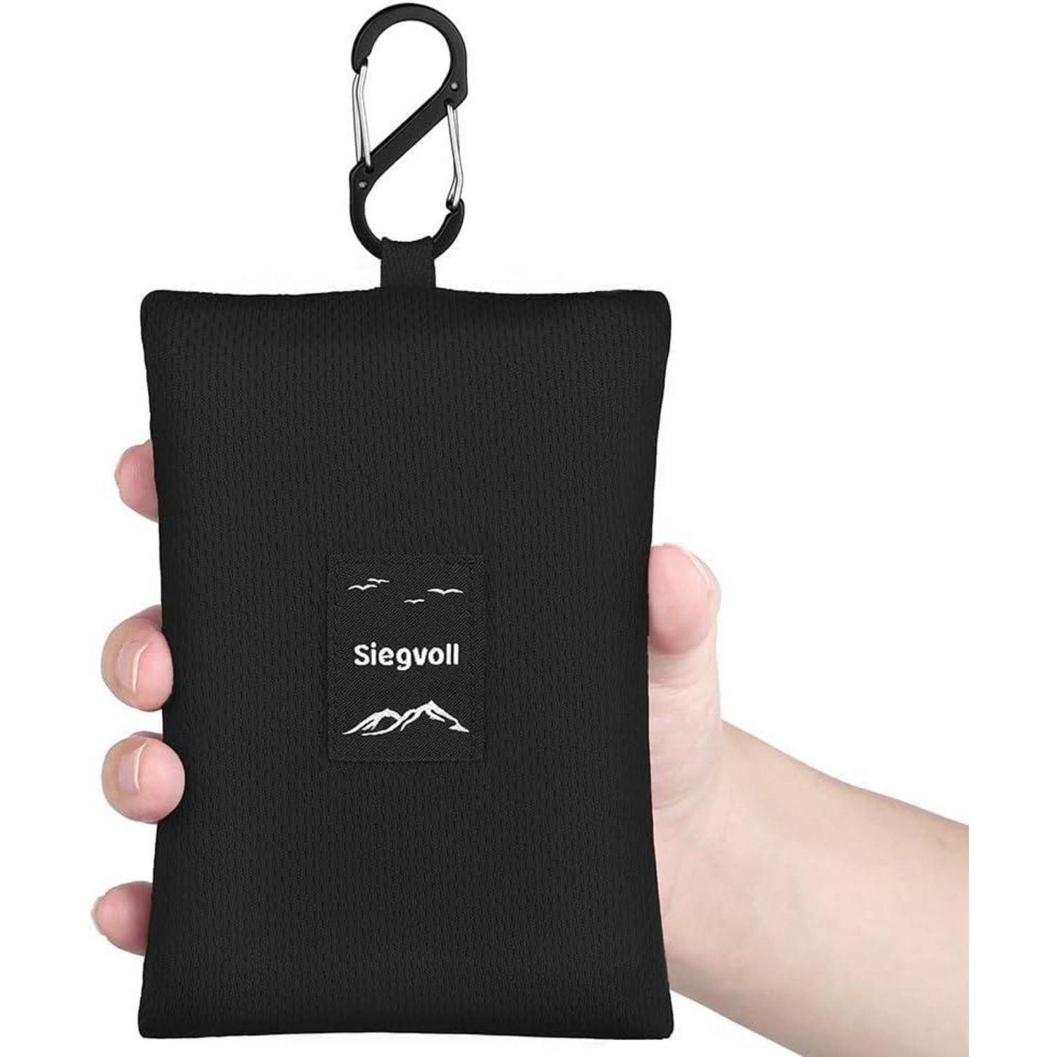 Eine Hand hält eine schwarze faltbare Tasche mit einem Karabinerhaken. Die Tasche weist ein Design mit Bergen und dem Wort 