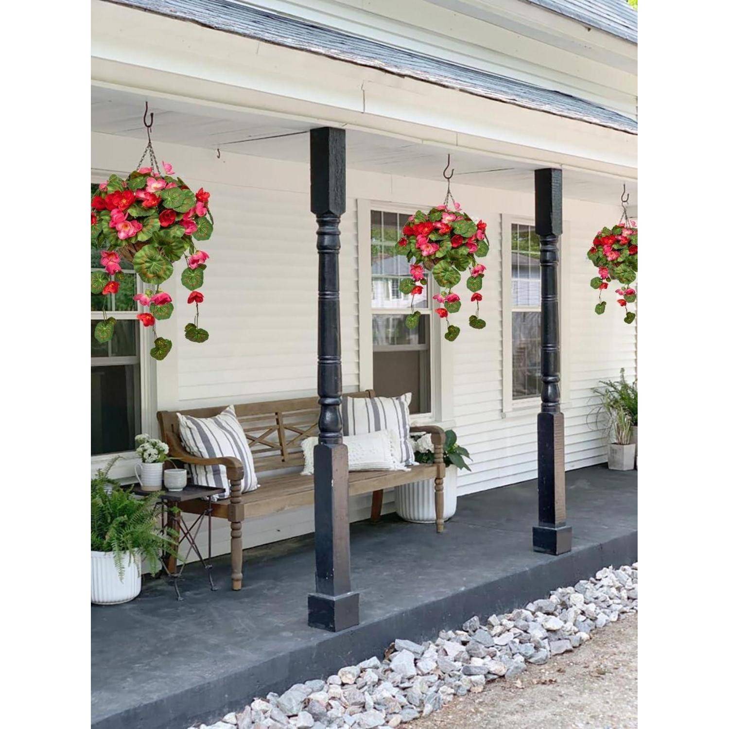 Eine Veranda mit einer Holzbank, gestreiften Kissen und hängenden roten Blumenkörben, gerahmt von schwarzen Säulen und einer Einfassung aus Steinen.