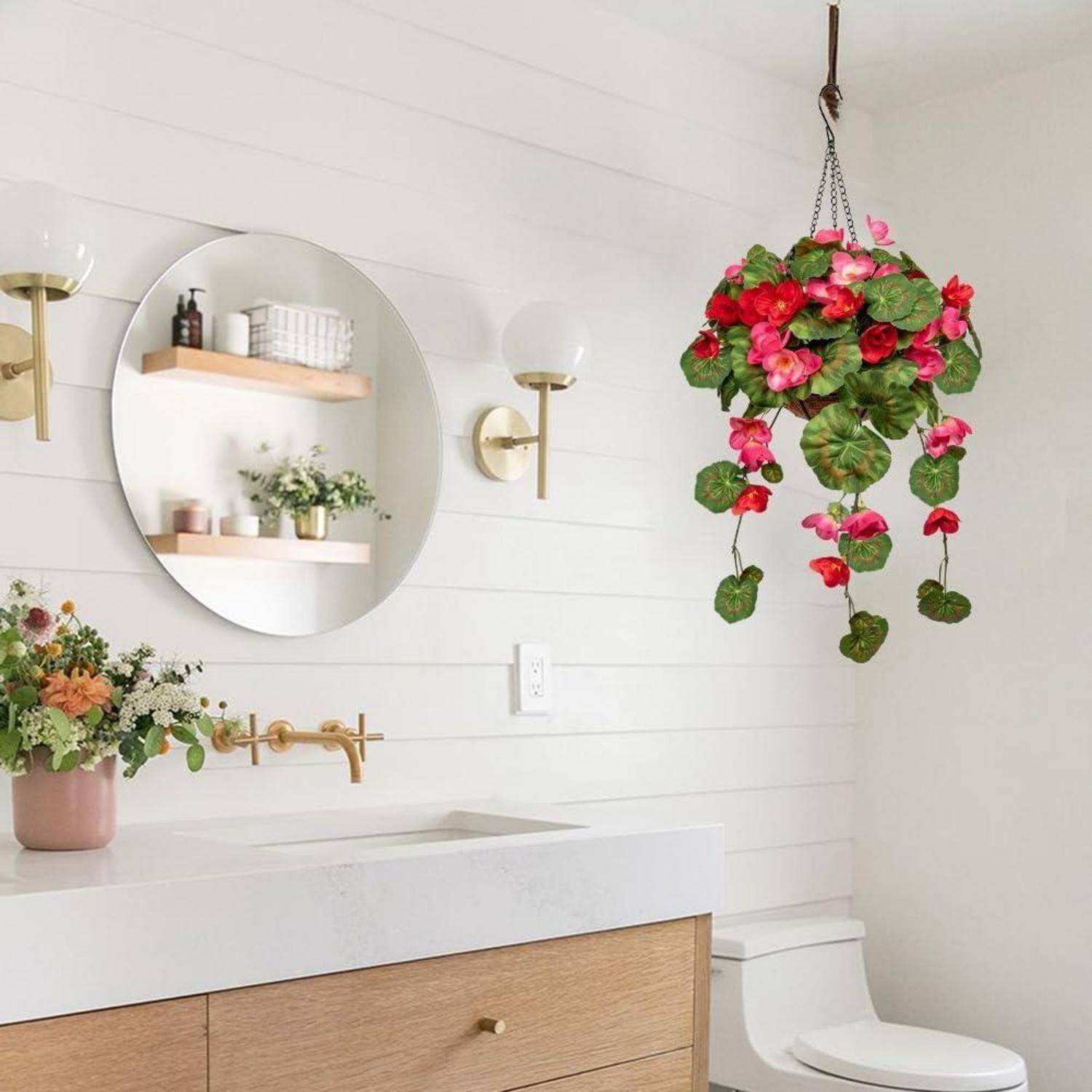 Ein modernes Badezimmer verfügt über einen runden Spiegel, eine wandmontierte Armatur, einen hängenden Korb mit rosa Blumen und eine minimalistische Dekoration auf den Regalen.