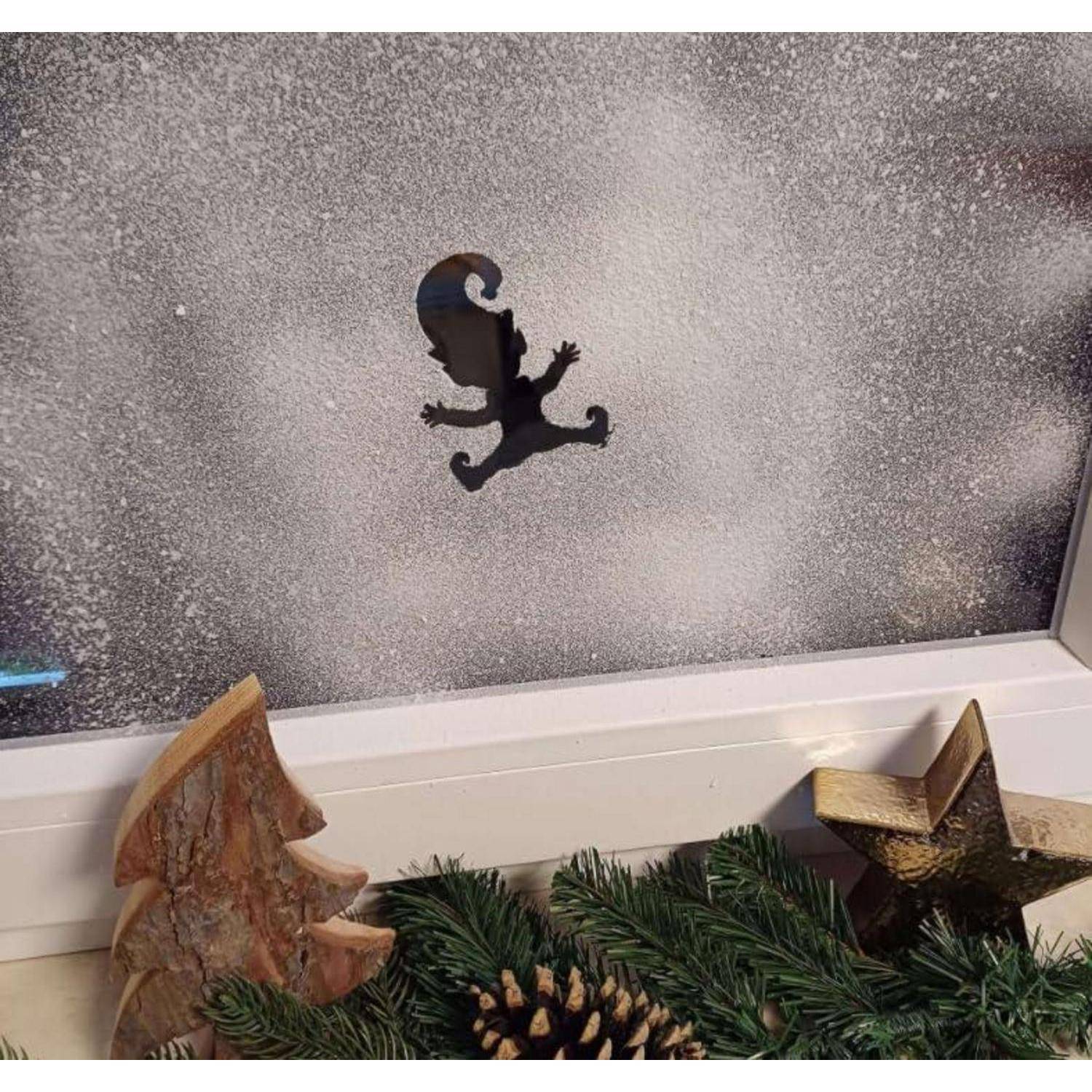Ein Eidechsenschatten auf einem verschneiten Fenster mit festlichen Dekorationen, einschließlich einer Tannenzapfen und kleiner Baumfiguren auf der Fensterbank.