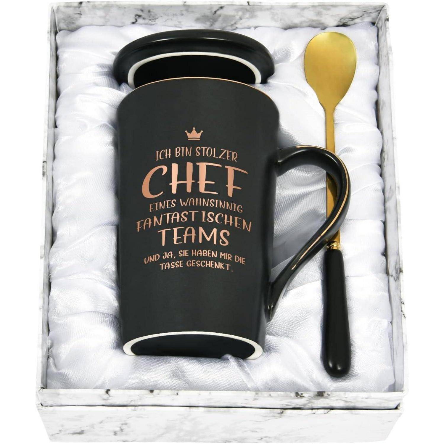 Eine schwarze Tasse mit goldener Schrift auf Deutsch, die den Text 'Ich bin stolzer Chef eines wahnsinnig fantastischen Teams' trägt, in einer Geschenkbox mit einem goldenen Löffel.