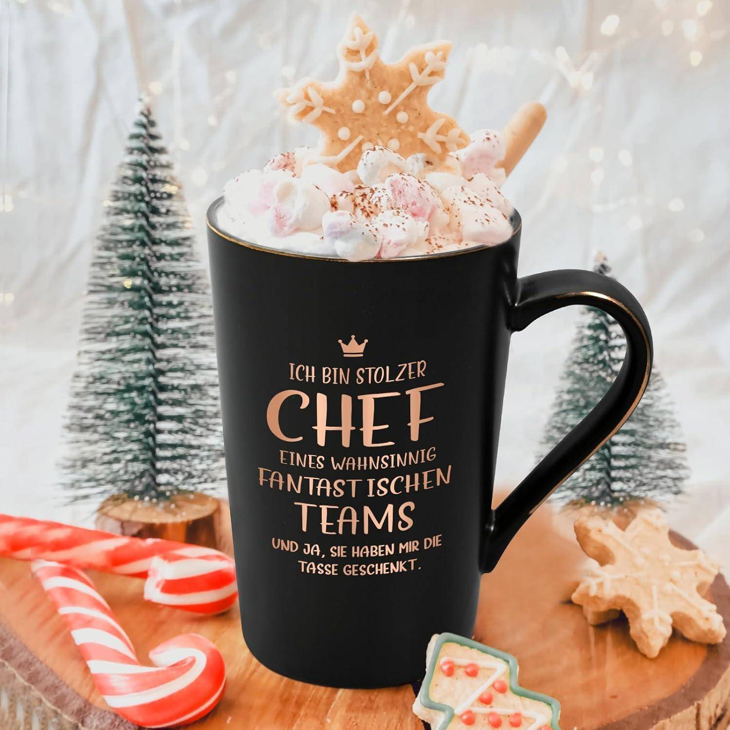 Eine Tasse gefüllt mit Schlagsahne und Lebkuchen, mit deutschem Text, der ein Team lobt. Umgeben von festlichen Plätzchen und kleinen Bäumen.