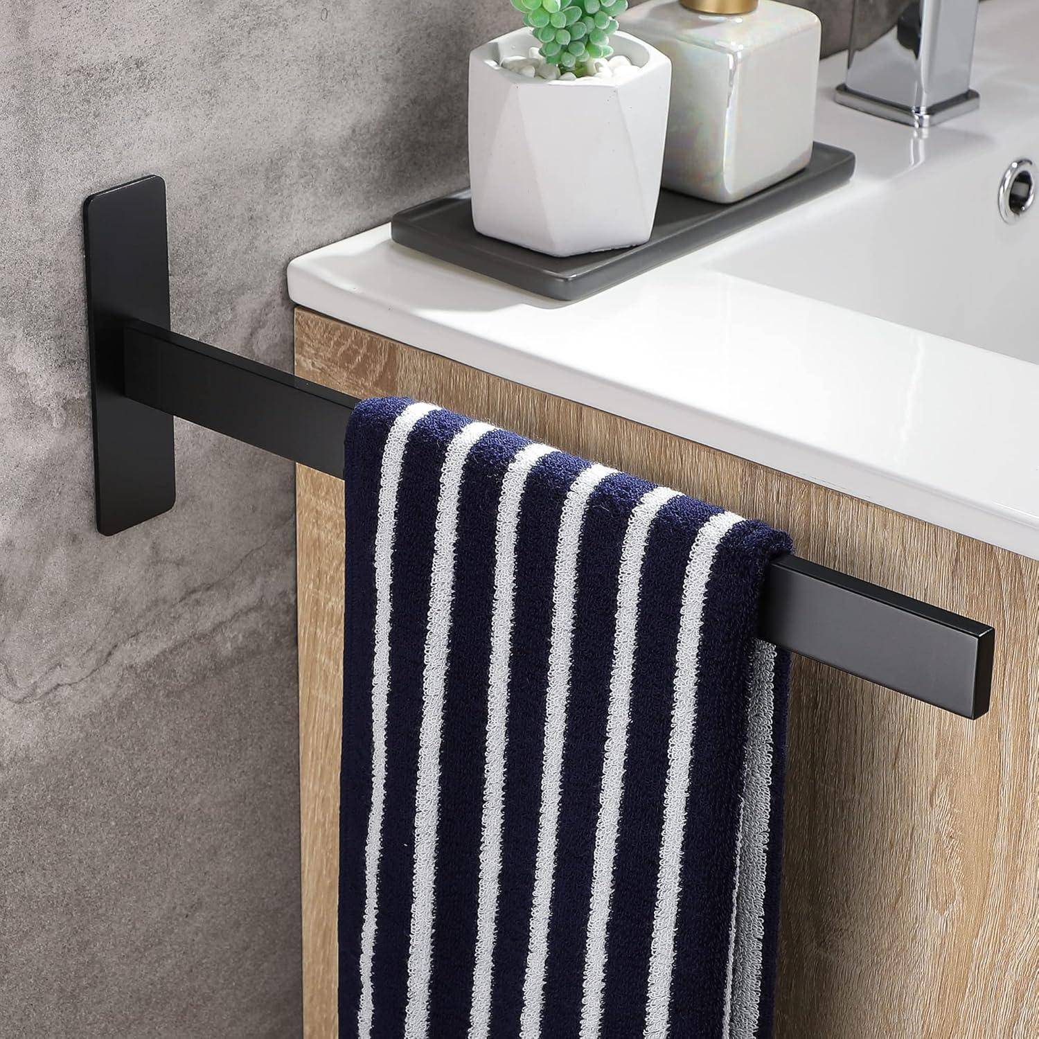 Ein modernes Waschbecken mit einem schwarz-weiß gestreiften Handtuch, das an einem schlanken schwarzen Handtuchhalter hängt. Eine kleine Pflanze und Toilettenartikel stehen neben dem Waschbecken.