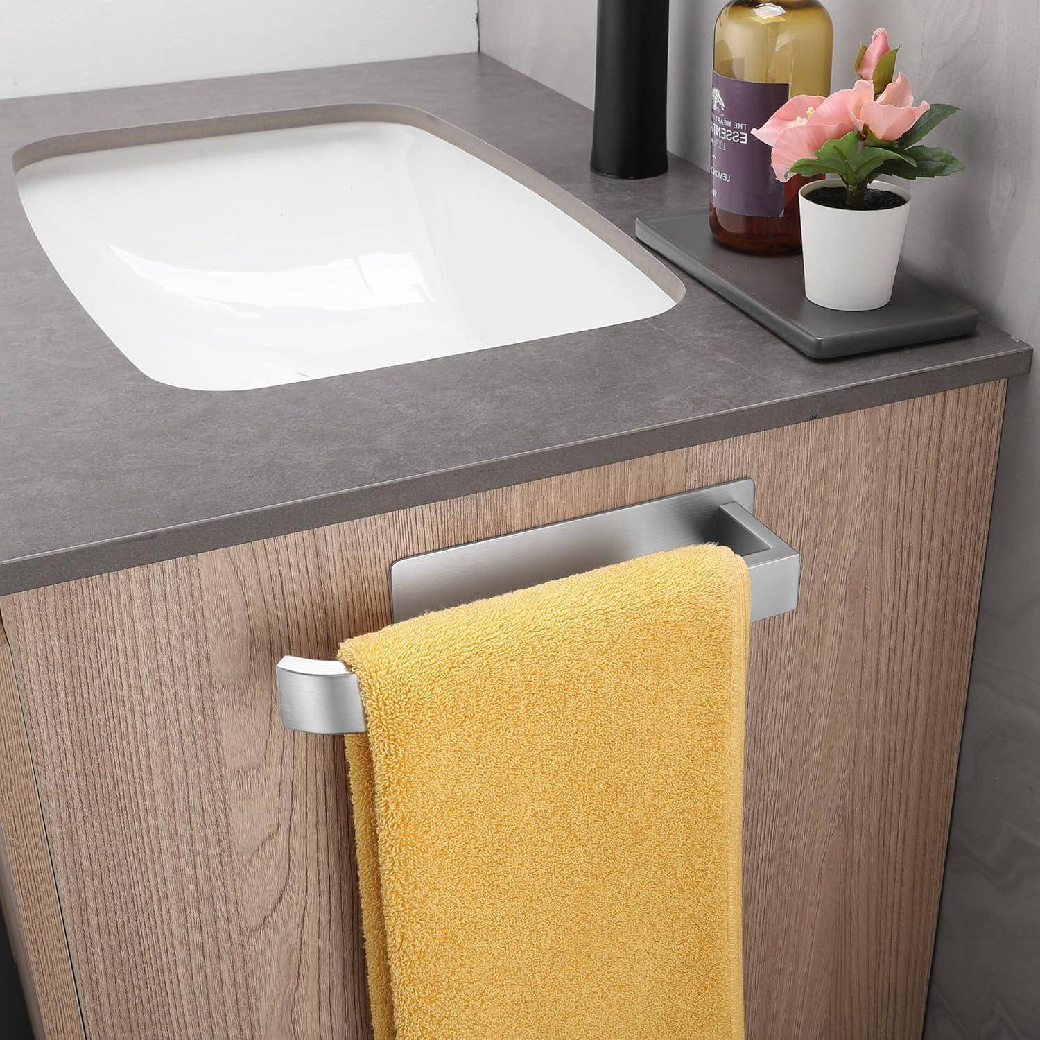 Badezimmerwaschtisch mit einem hellholzfarbenen Schrank, einem gelben Handtuch, das an einer silbernen Stange hängt, sowie einer Arbeitsplatte mit einer Seifenflasche und einer kleinen Topfpflanze.