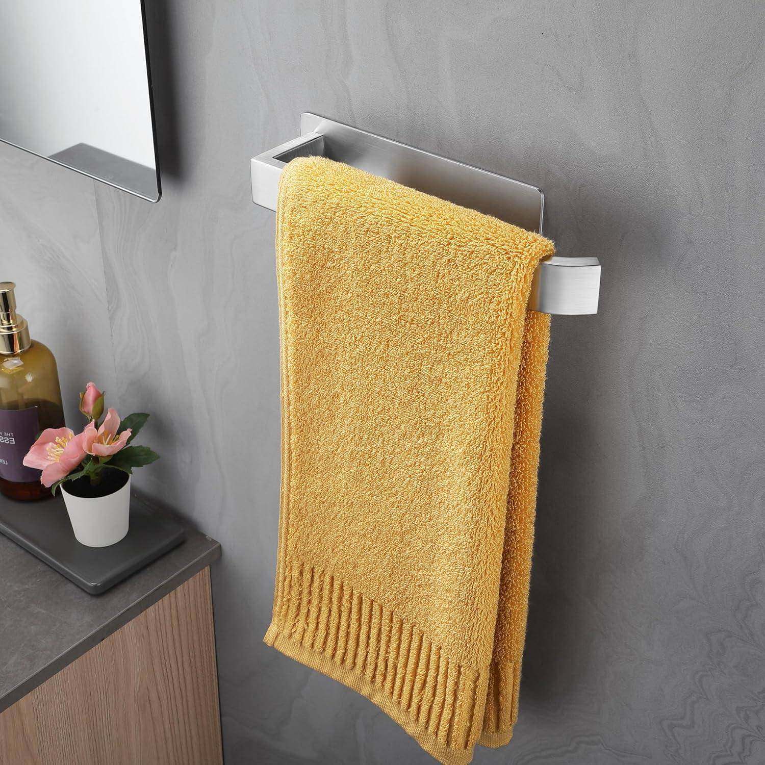Ein Badezimmer zeigt ein gelbes Handtuch auf einem Metallgestell, eine Arbeitsplatte mit einer kleinen Topfpflanze und einem Seifenspender.