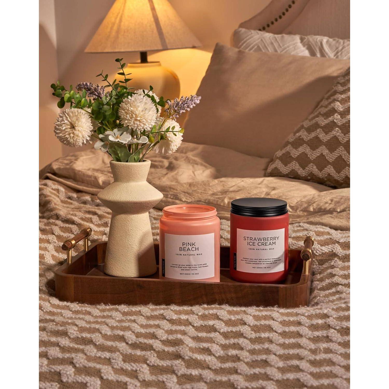 Ein Holztablett auf einem Bett trägt eine Vase mit Blumen und zwei Kerzen mit den Aufschriften 