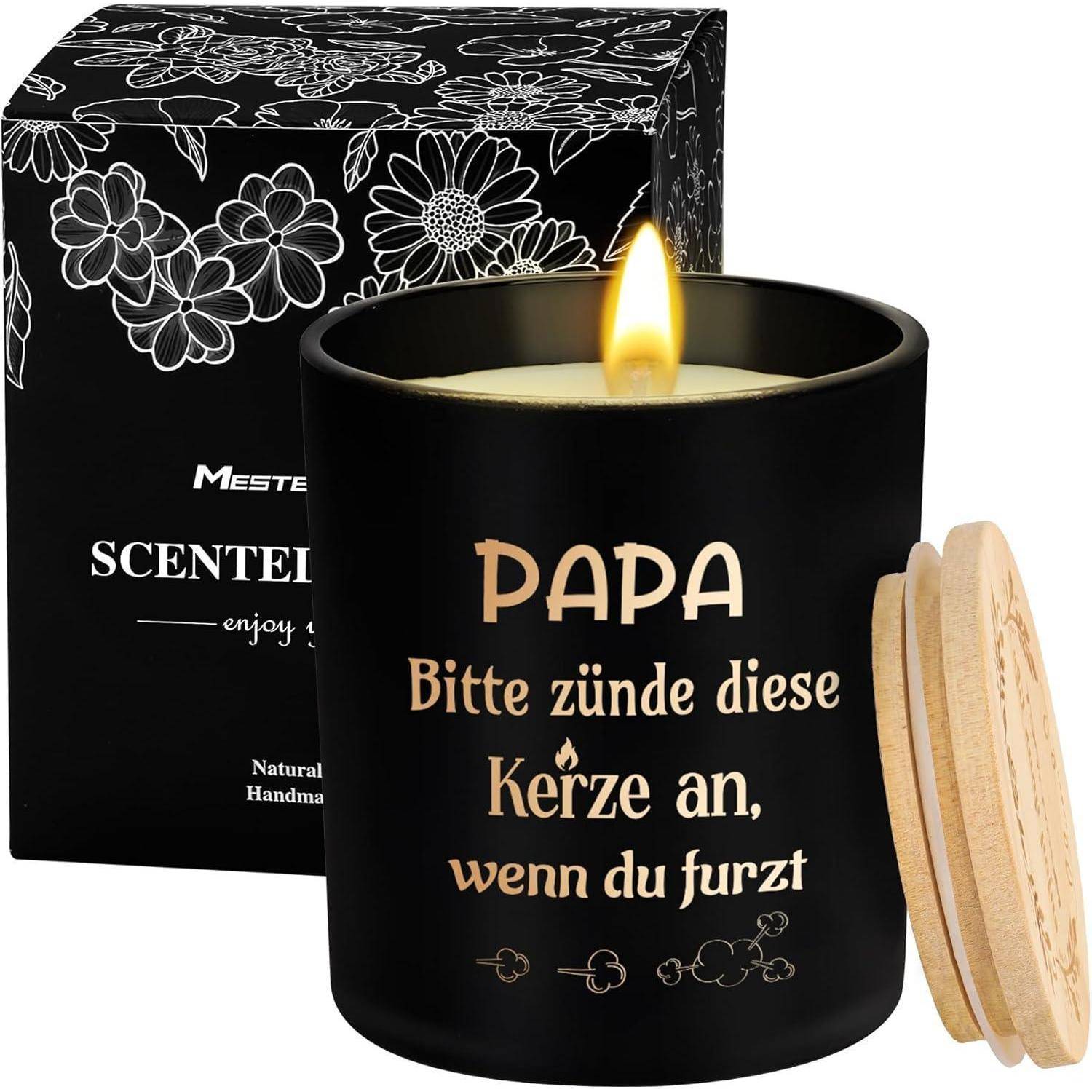 Eine brennende Kerze in einem schwarzen Glas mit deutschem Text: 'Papa, bitte zünde diese Kerze an, wenn du furzt.' Die Kerze hat einen Holzdeckel in der Nähe.